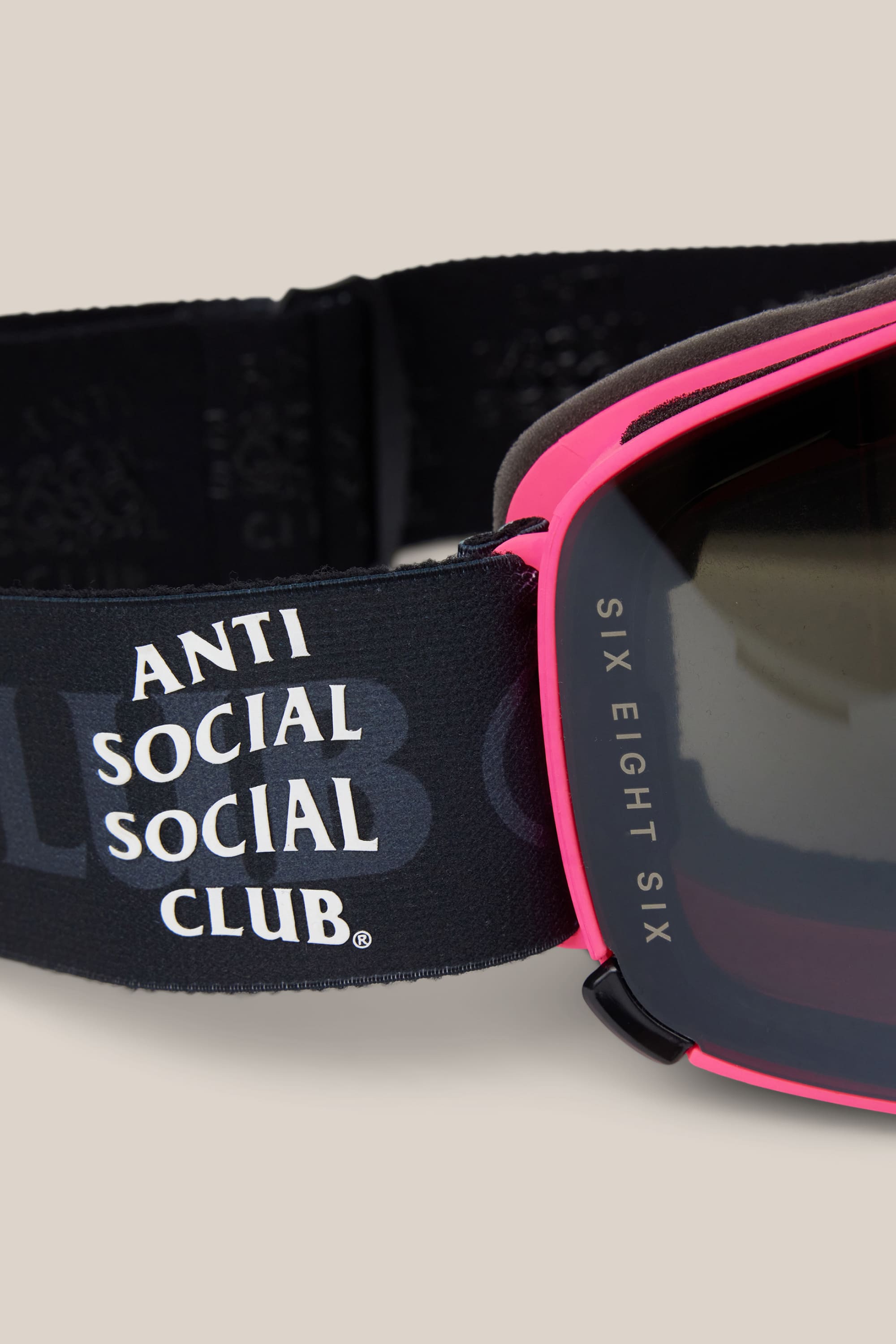 Close-up of 686 SMARTY® Magnetic Goggle in black with a pink frame. The strap displays "ANTI SOCIAL SOCIAL CLUB" in white, and "SIX EIGHT SIX" is printed on the lens. Light beige background. Brand: 686.