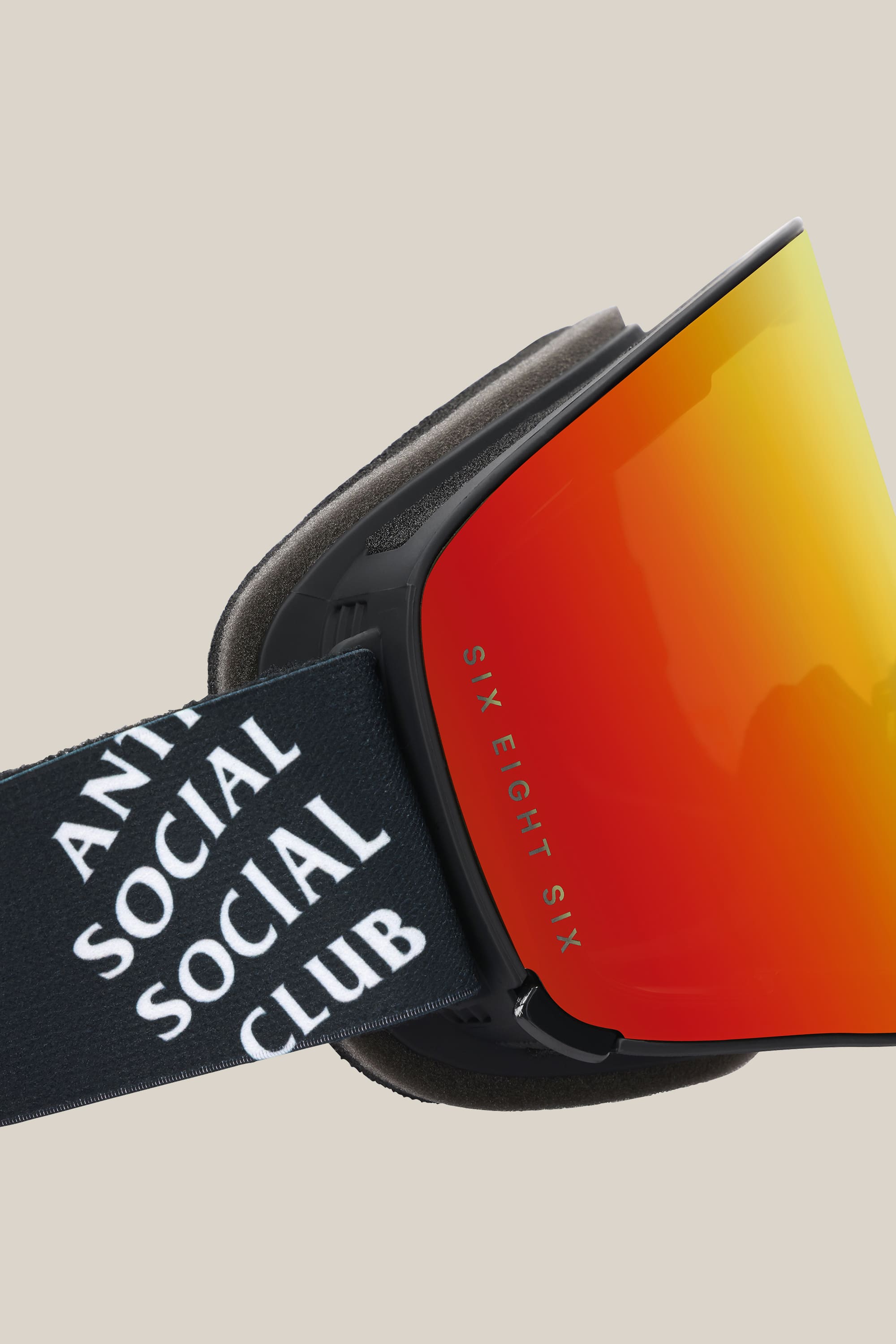A close-up of the 686 SMARTY® Magnetic Goggle shows a reflective orange lens and a black strap with white ANTI SOCIAL SOCIAL CLUB text. The lens side reads SIX EIGHT SIX. The background is beige. Brand: 686.