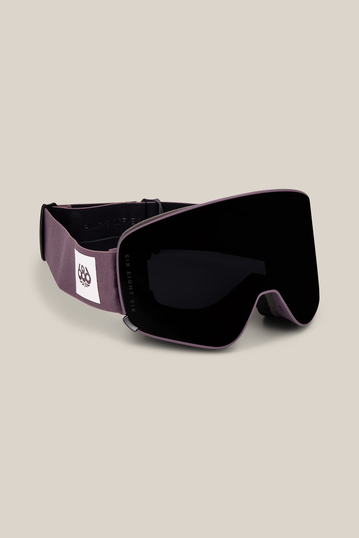 The 686 SMARTY® Magnetic Goggle by 686 features a black lens and a grayish-purple strap adorned with a white patch displaying a black geometric logo, showcased against a light beige background.