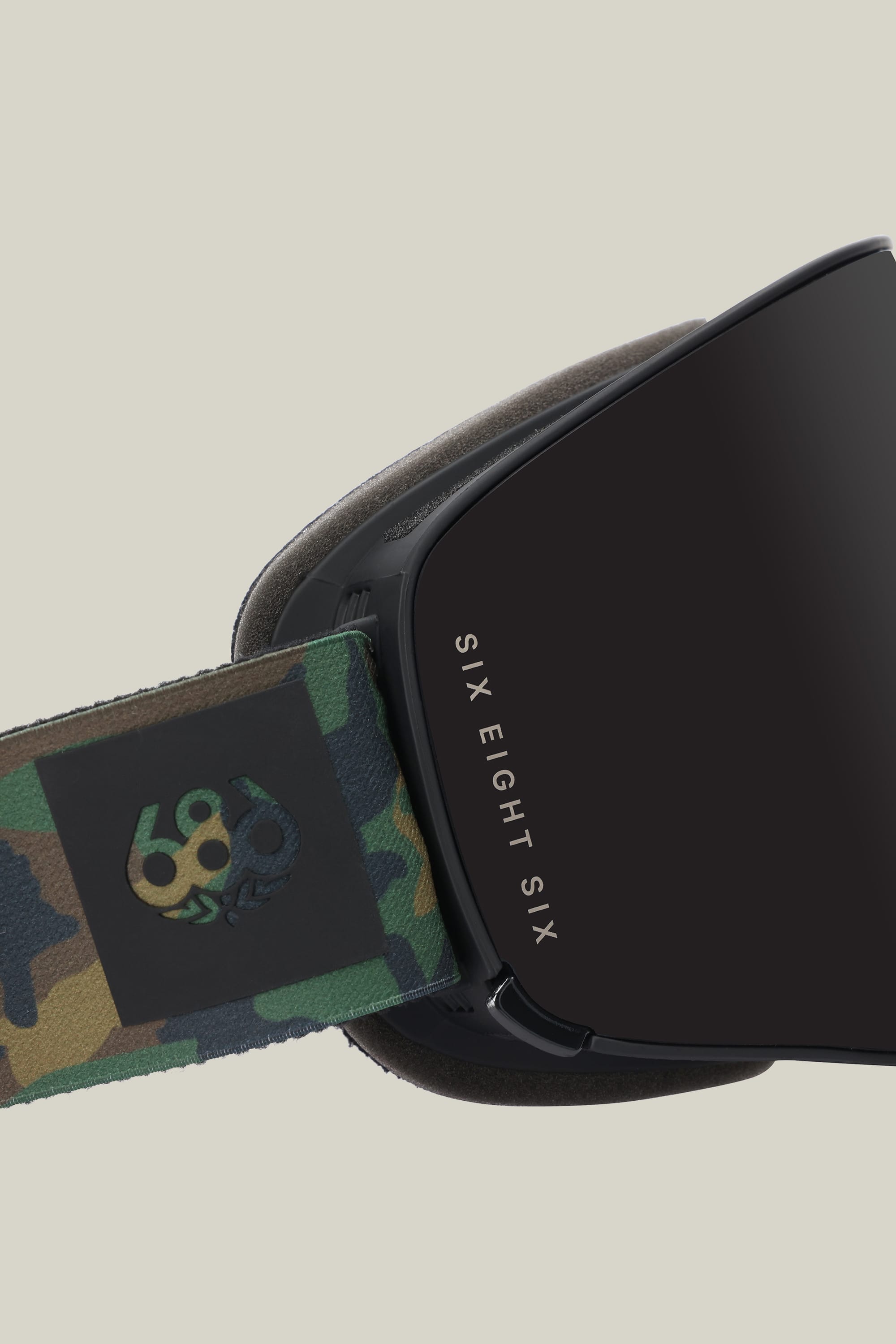 Close-up of the 686 SMARTY® Magnetic Goggle displaying 686 text on the lens and a camo-patterned strap with a 686 logo, set against a plain light beige background.