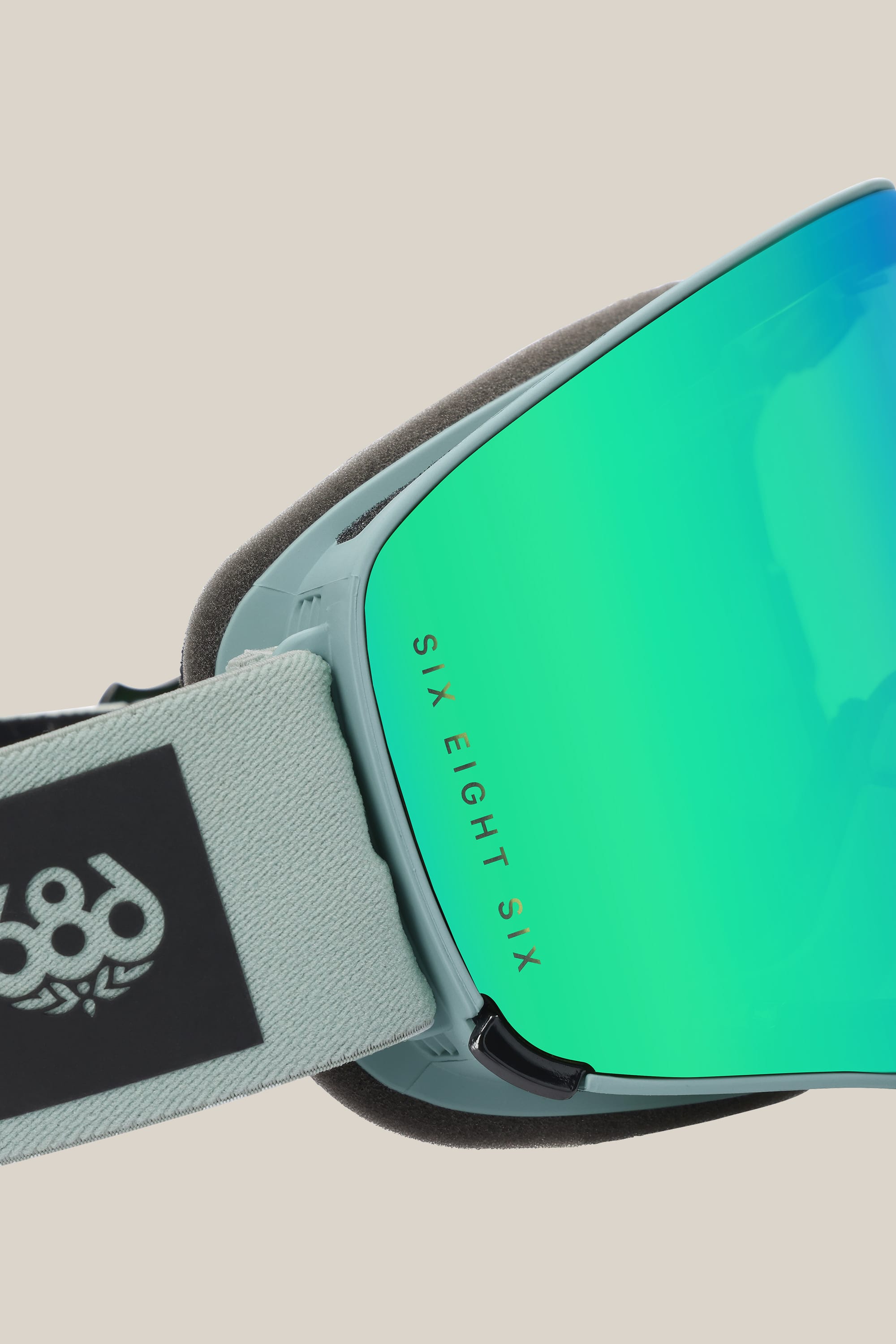 Close-up of the 686 SMARTY® Magnetic Goggle, a minimalist design with reflective blue-green magnetic lenses and a light gray strap bearing the 686 logo and SIX EIGHT SIX branding on the lens frame.