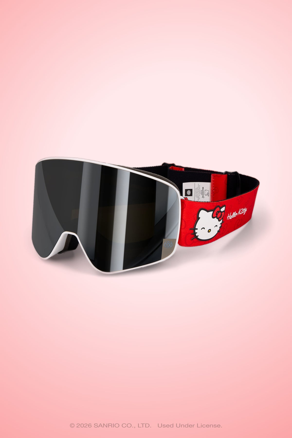 The 686 SMARTY® Magnetic Goggle by 686 features a black, full-lens vision lens and a red strap accented with a Hello Kitty face and logo, showcased against a pink gradient backdrop.