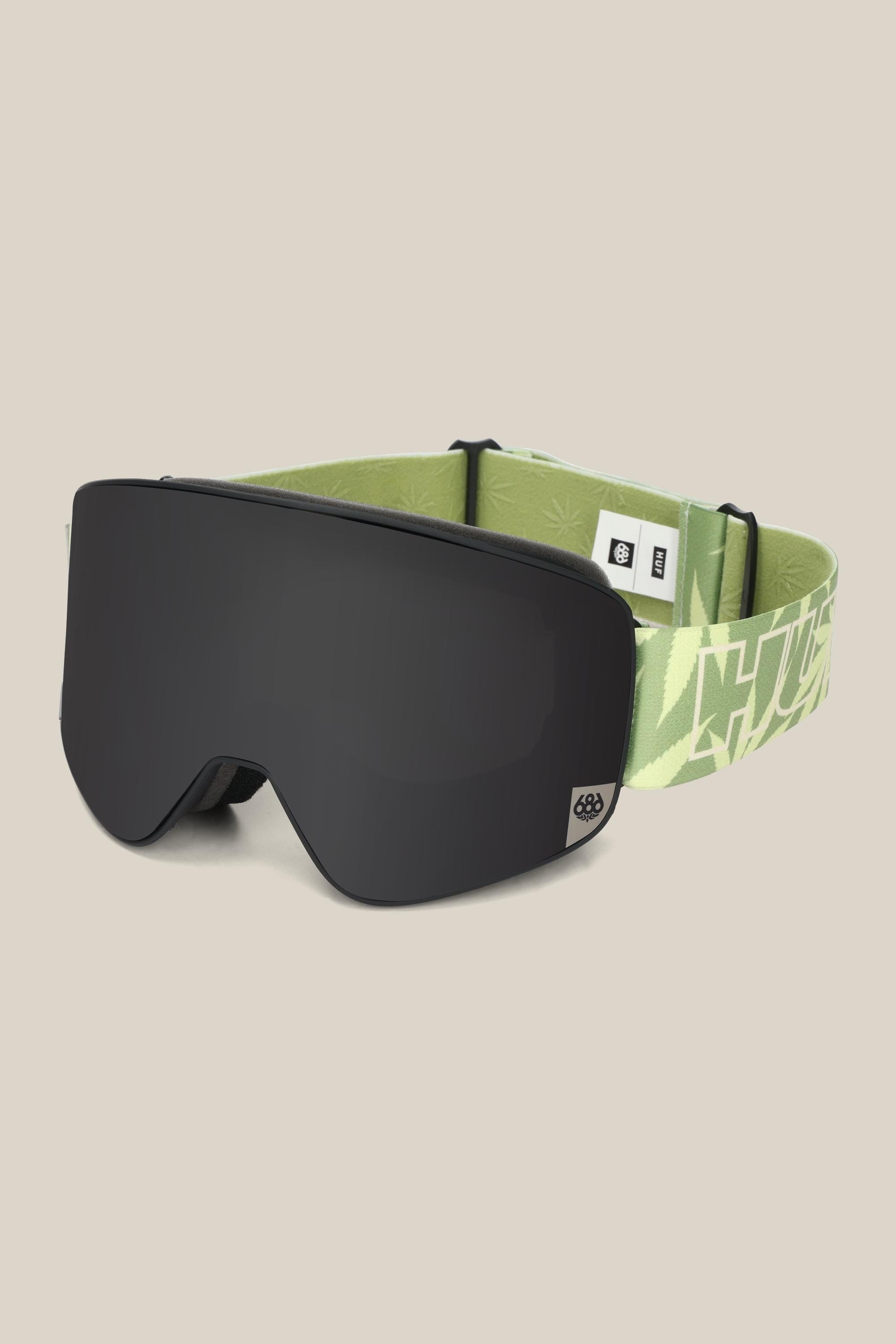The 686 SMARTY® Magnetic Goggle by 686 features a sleek black minimalist design, a dark frameless magnetic lens, and a light green adjustable strap with subtle graphic patterns and small logos.