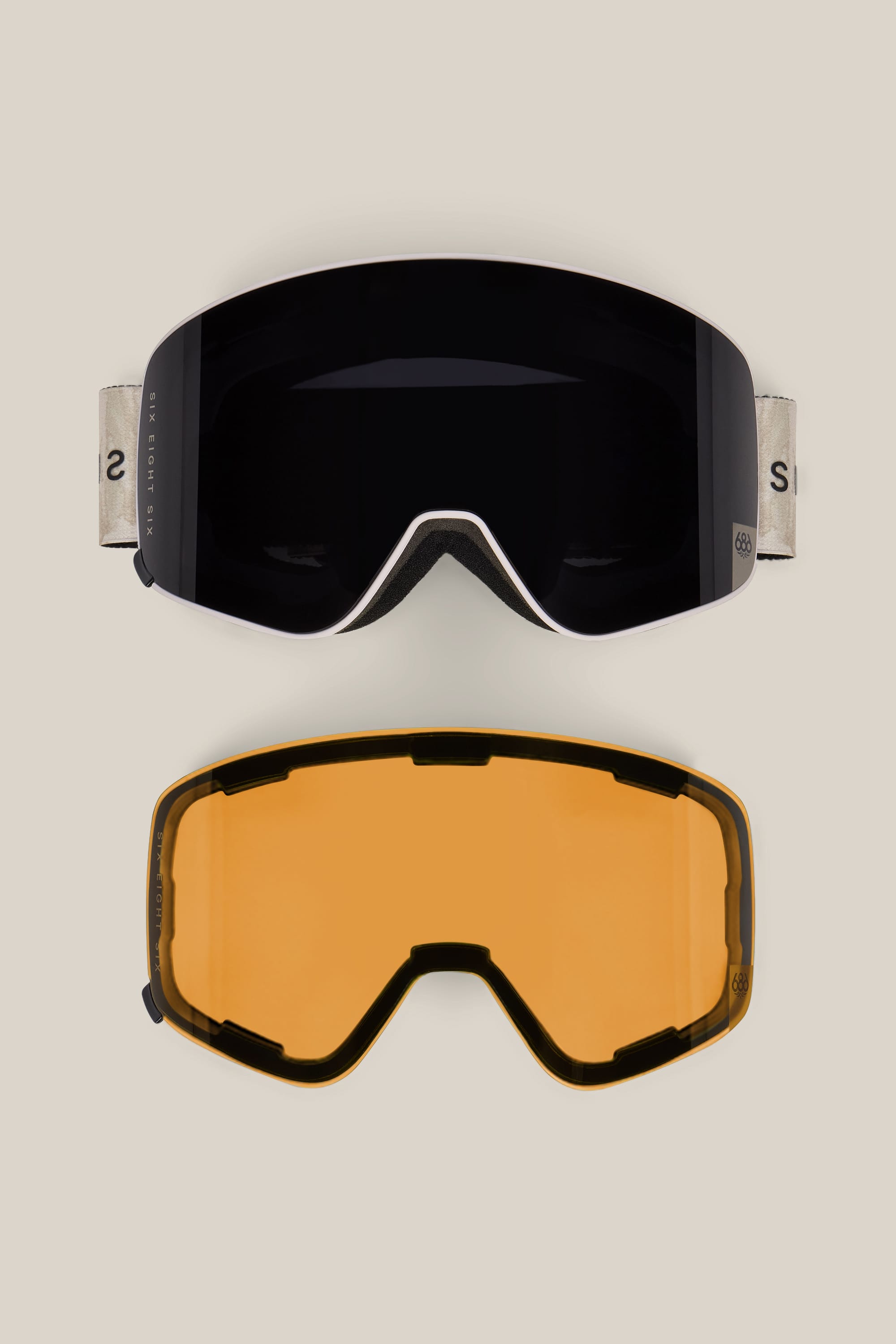 The 686 SMARTY® Magnetic Goggle by 686, featuring a black lens and beige strap, is displayed above a separate, interchangeable amber lens on a neutral background.