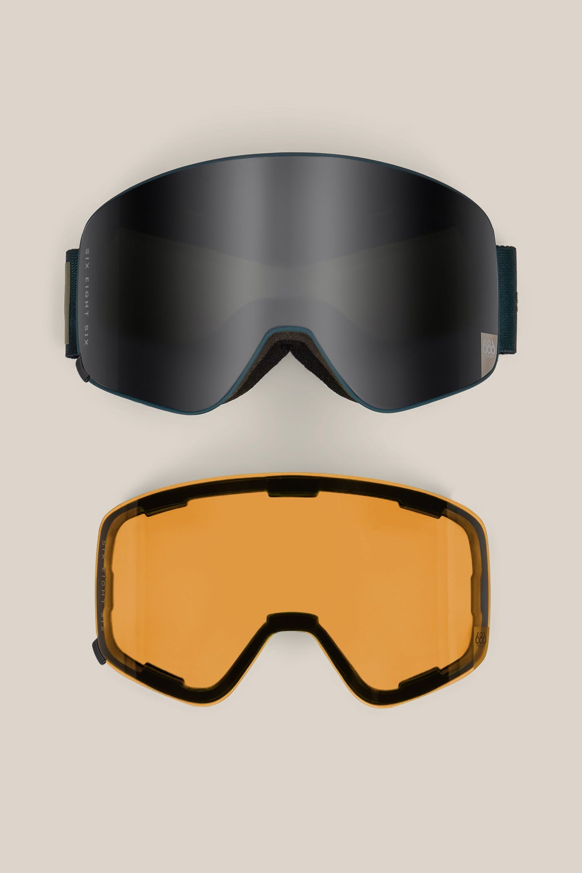 A pair of 686 SMARTY® Magnetic Goggles in black, along with an additional interchangeable amber lens displayed beneath them, both set against a neutral beige background.