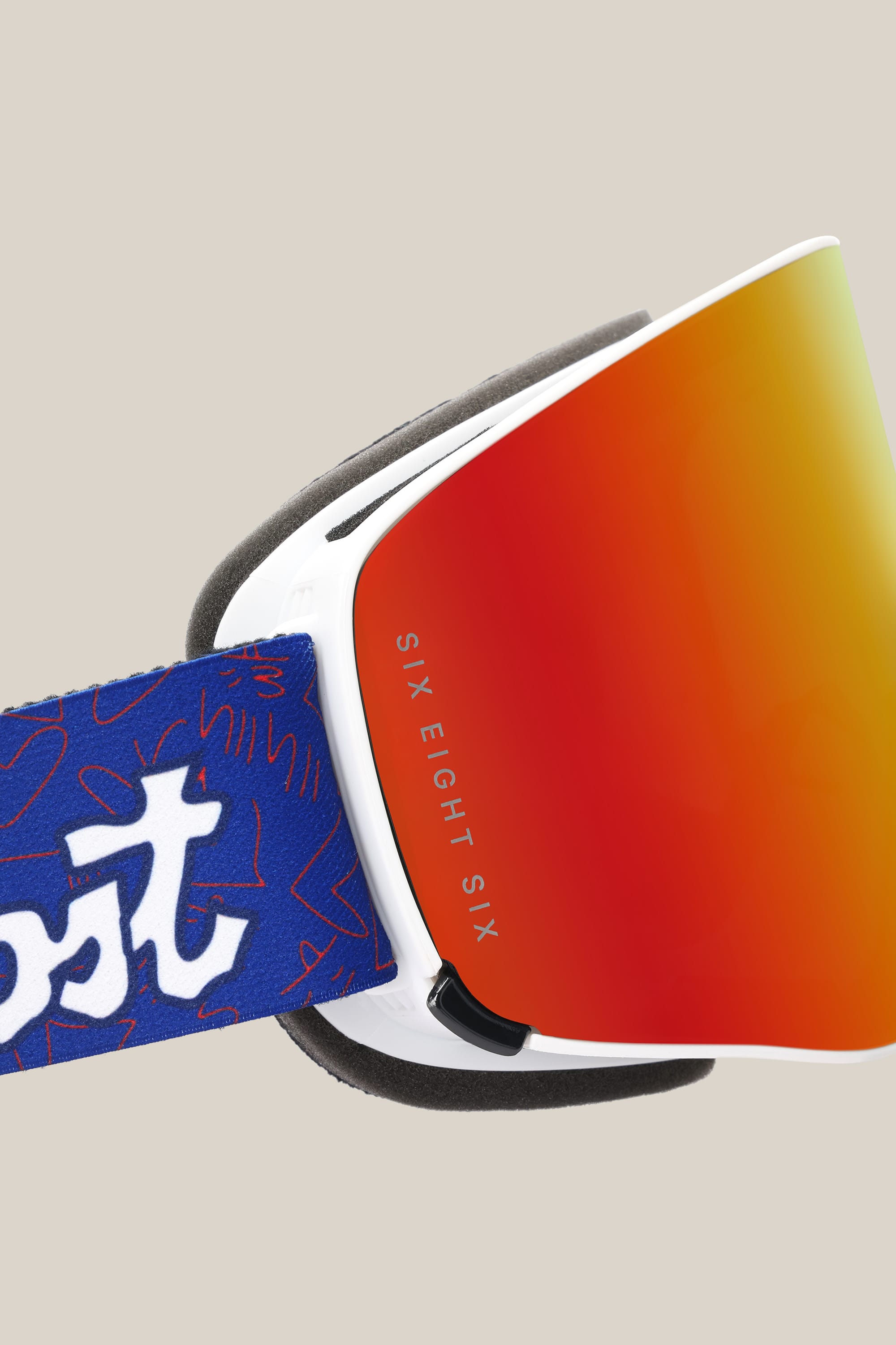 A close-up of the 686 SMARTY® Magnetic Goggle shows its red-orange reflective lens with "SIX EIGHT SIX" text, a white frame, and a blue strap with abstract white and red patterns and branding from 686.