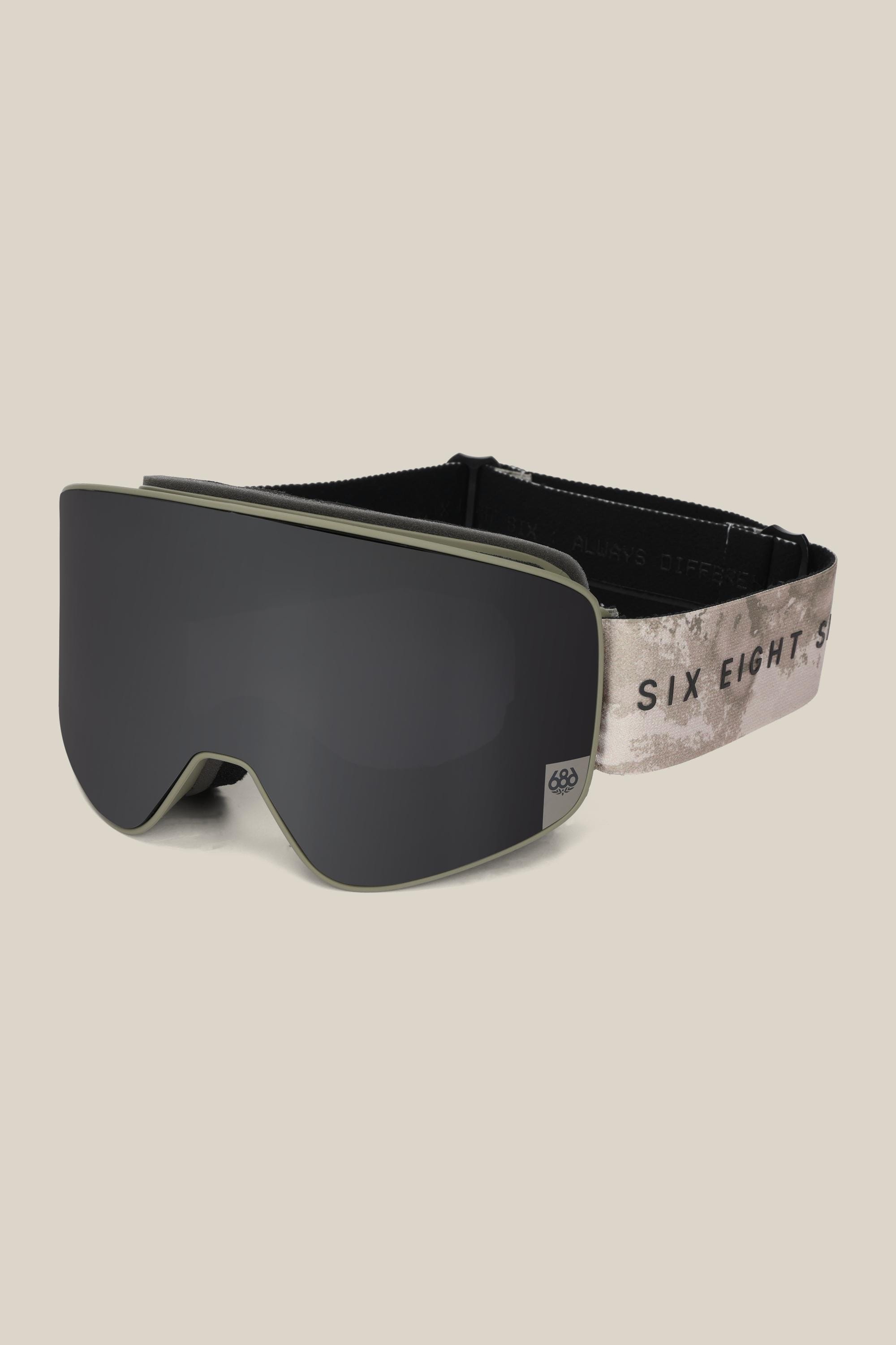 The 686 SMARTY® Magnetic Goggle by 686 features a sleek black frame, wide dark lens, and an adjustable beige, black, and gray strap with "SIX EIGHT" text, shown in a minimalist design against a plain light background.