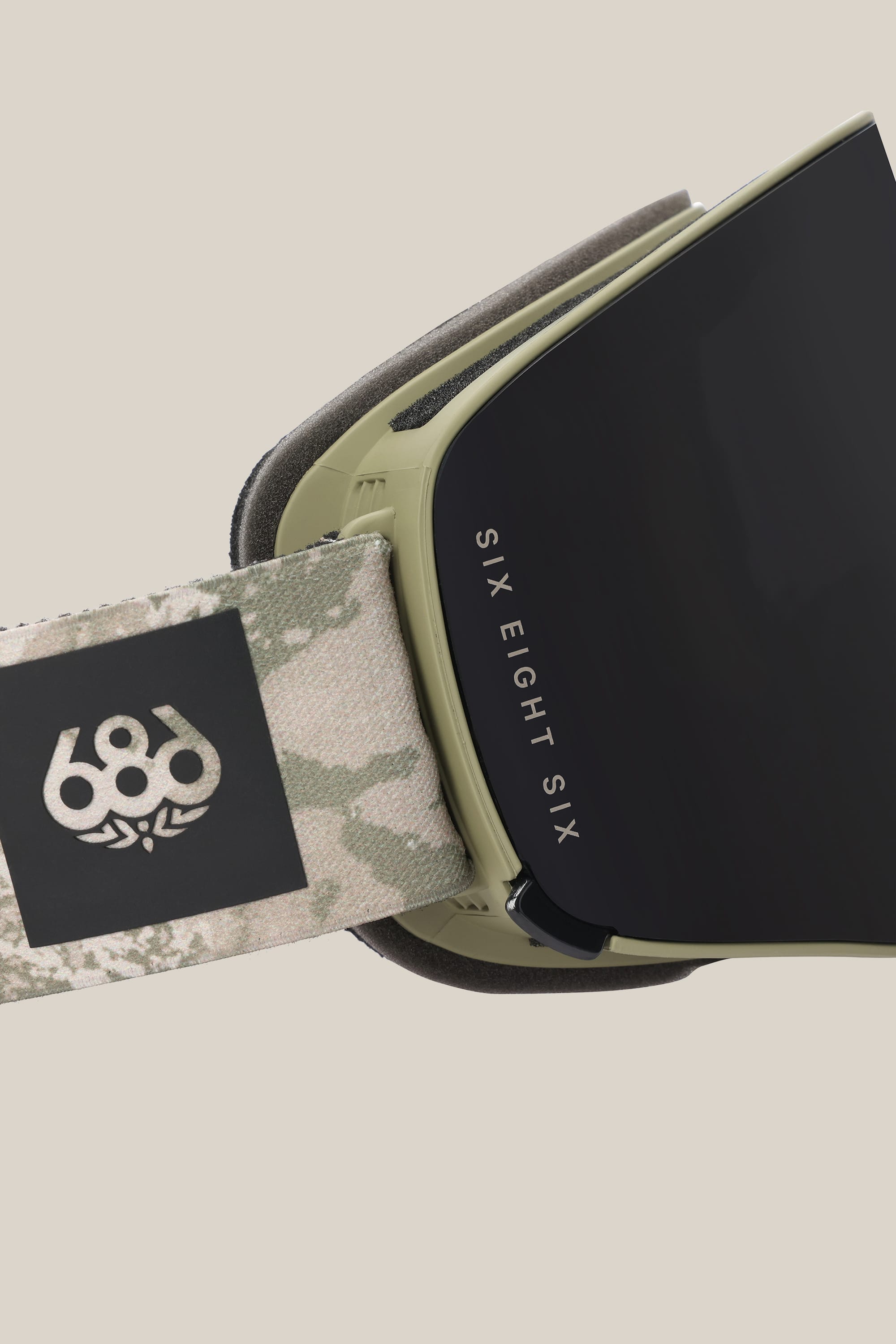 Close-up of the 686 SMARTY® Magnetic Goggle—a minimalist style featuring a matte black lens, green frame, and camo strap with the white 686 logo and "SIX EIGHT SIX" text on the side.