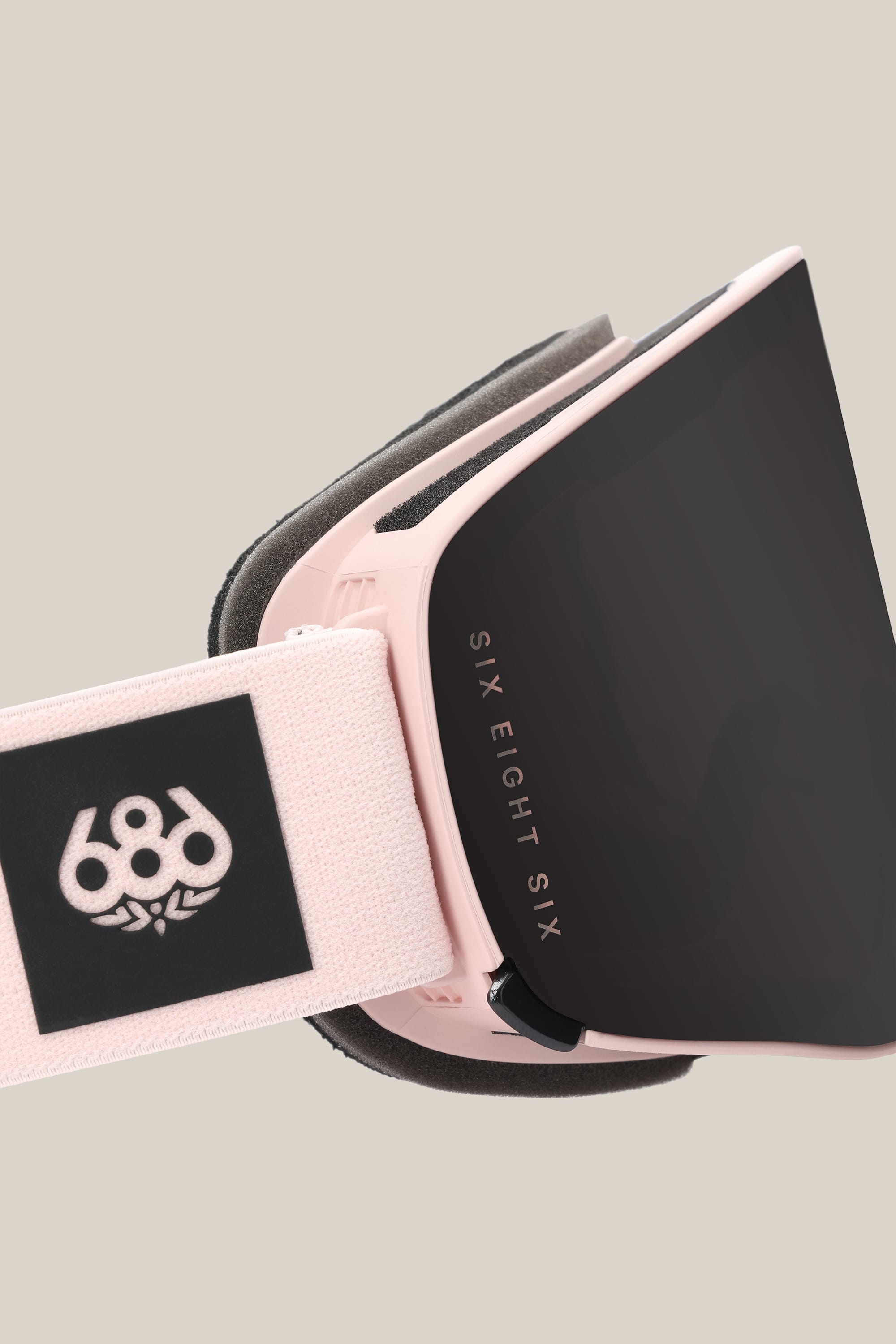 A close-up of the 686 SMARTY® Magnetic Goggle in pink with a black lens, featuring SIX EIGHT SIX text on the frame and a 686 logo on the white strap, set against a plain beige background.