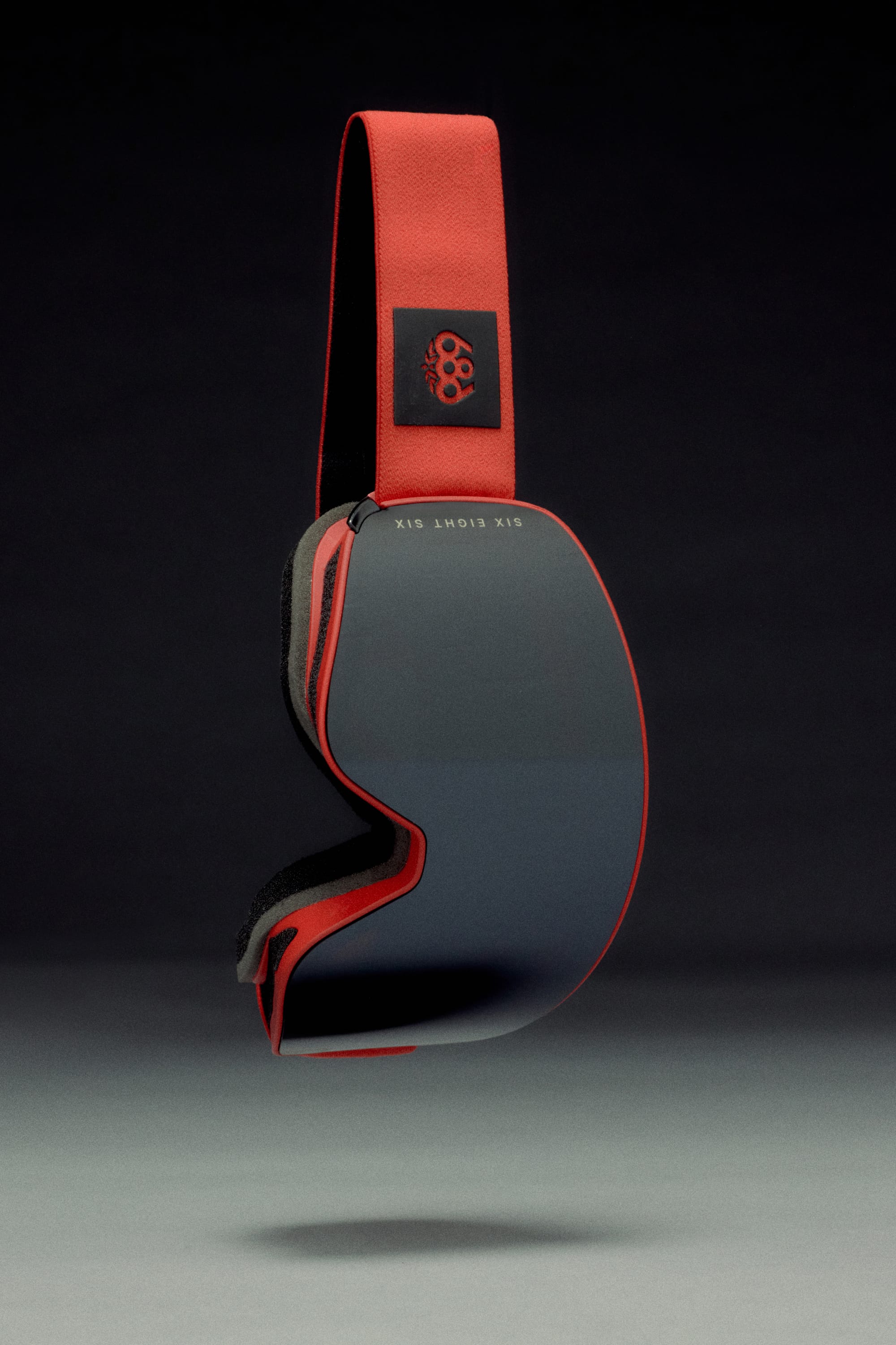 The 686 SMARTY® Magnetic Goggle by 686 features a reflective dark lens and a red strap with a black logo, displayed against a dark background for a sleek, minimalist look.