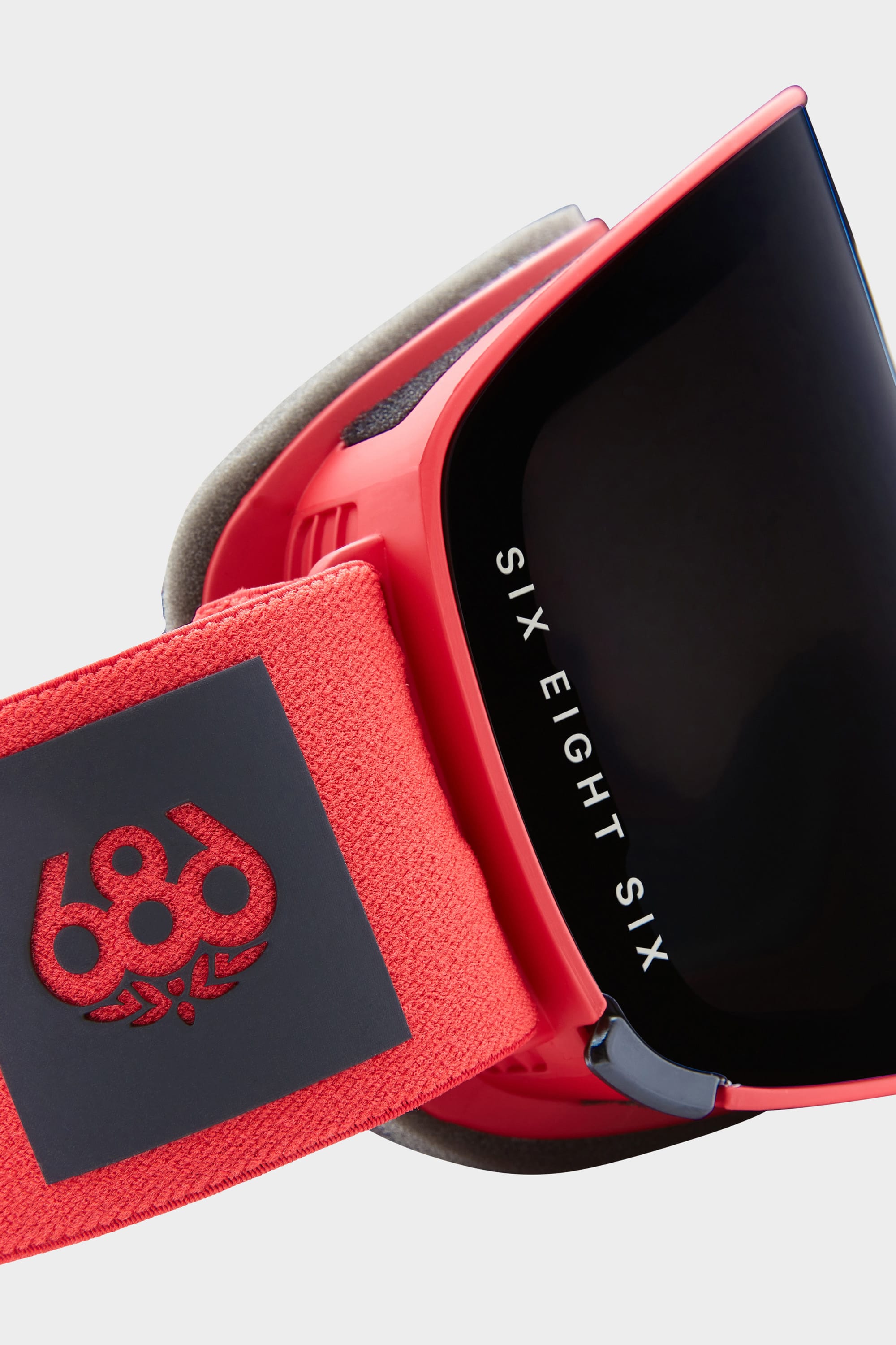 Close-up of the 686 SMARTY® Magnetic Goggle with a red frame and black lens. The strap shows a red 686 logo on black, and SIX EIGHT SIX is printed in white on the interchangeable lenses.