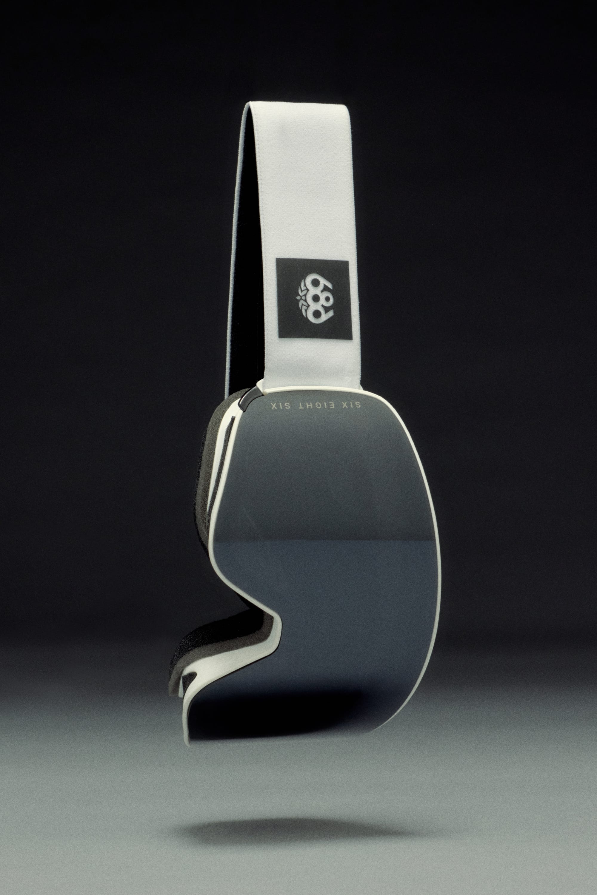 The 686 SMARTY® Magnetic Goggle by 686 features a sleek, modern design with a reflective dark lens, white strap, and interchangeable lenses, shown against a dark gradient background.