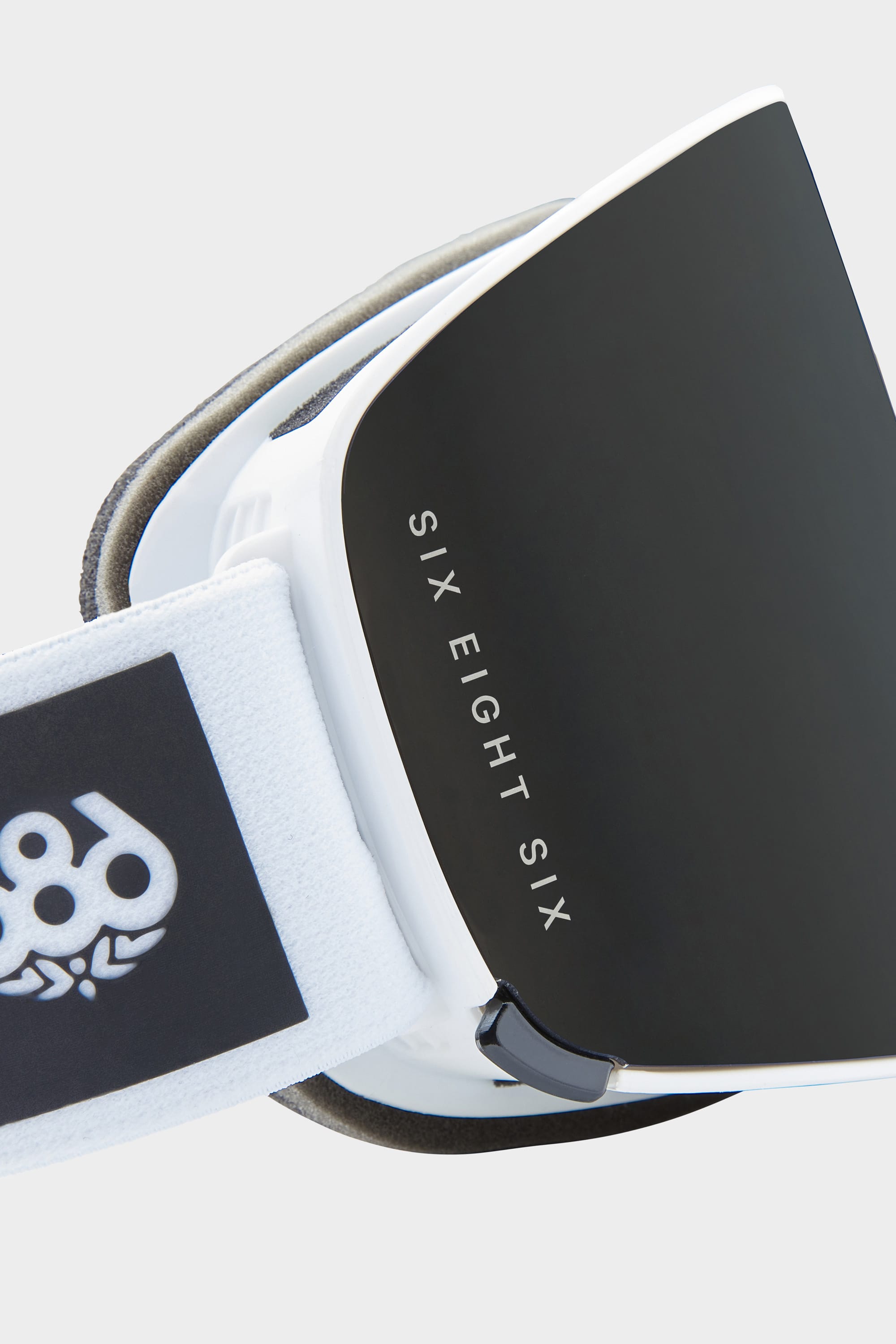 Close-up of the 686 SMARTY® Magnetic Goggle, a black and white minimalist design with a reflective lens featuring "SIX EIGHT SIX" text and the 686 logo on its white strap.