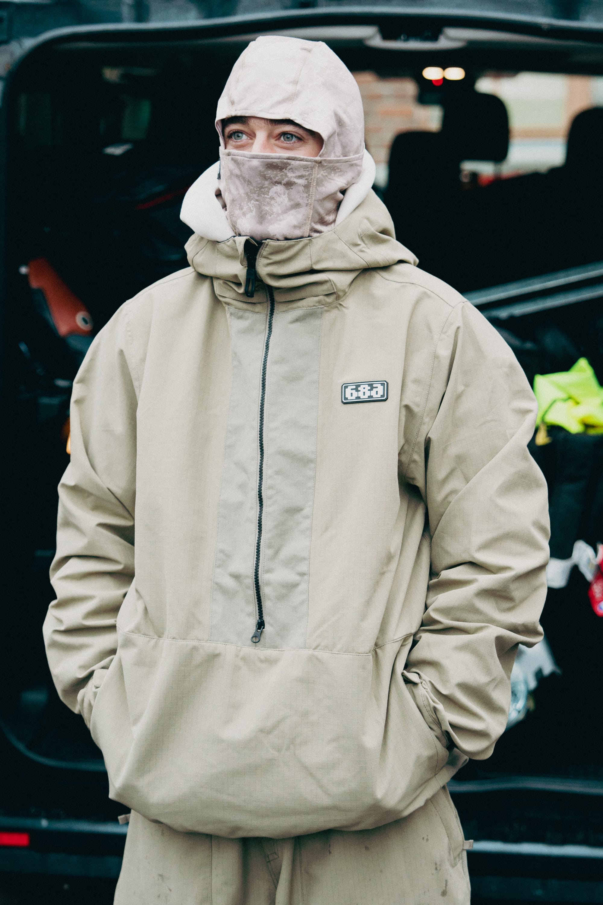 A person wearing the 686 Men's Ghost™ 2.5L Anorak in beige, along with a matching balaclava, stands with hands in pockets by an open vehicle trunk, looking slightly to the side.