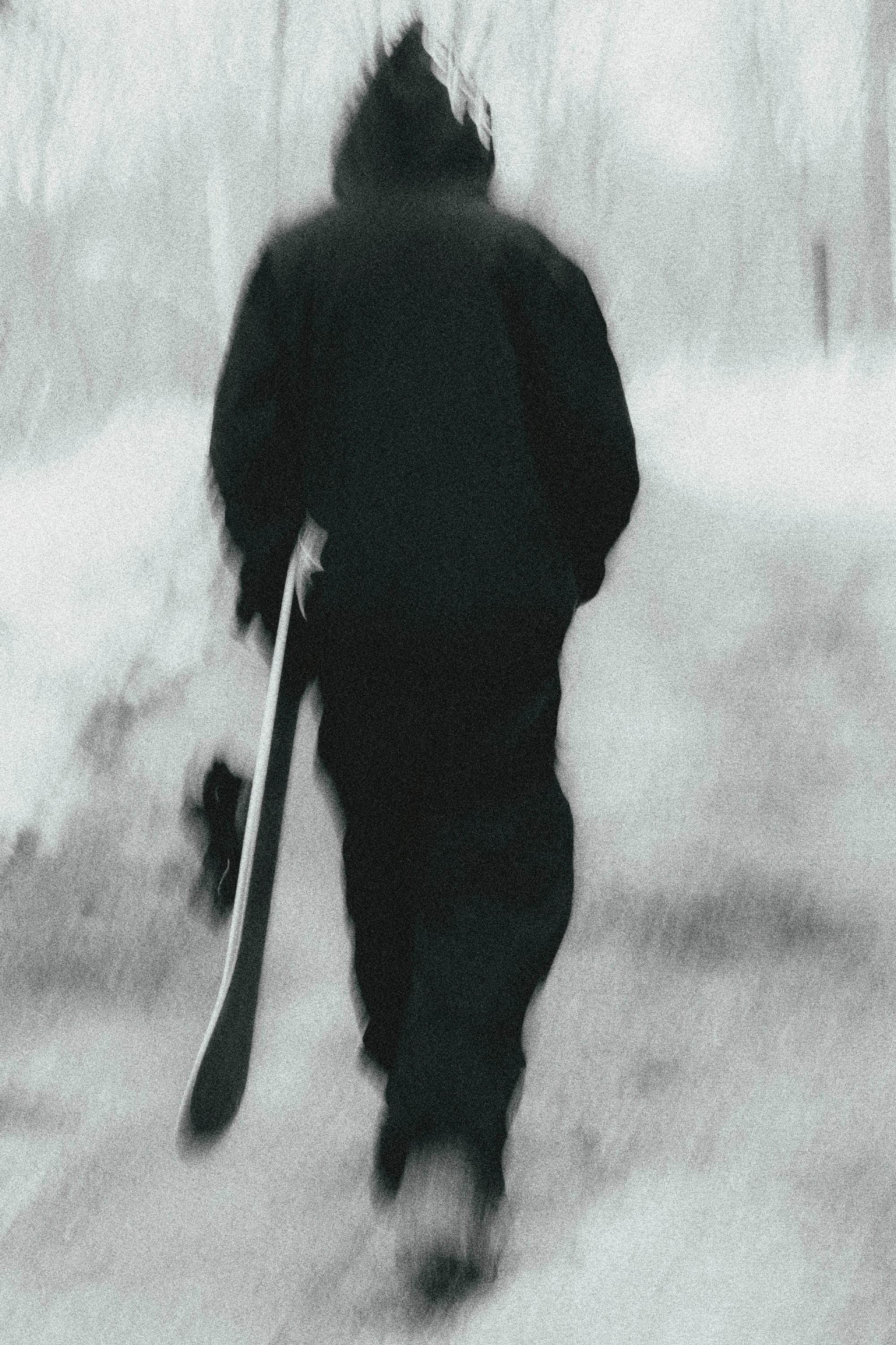 Wearing the 686 Ghost™ 2.5L Pant by 686, a person in dark winter clothes strolls down a snowy path with a snowboard in hand. The blurred image adds a dreamy, ethereal vibe to the scene.