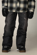 A person wearing a black and white plaid shirt, black snowboard gloves, 686 Men's Deconstructed™ Denim Pant by 686, and black snowboard boots stands against a neutral background.