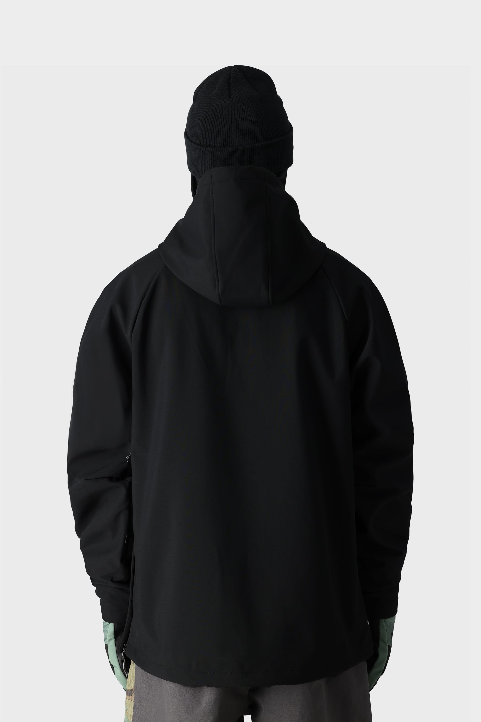A person wearing the 686 Men’s Waterproof Hoody by 686, along with a black beanie, green gloves, and gray pants, stands facing away from the camera against a plain light background.