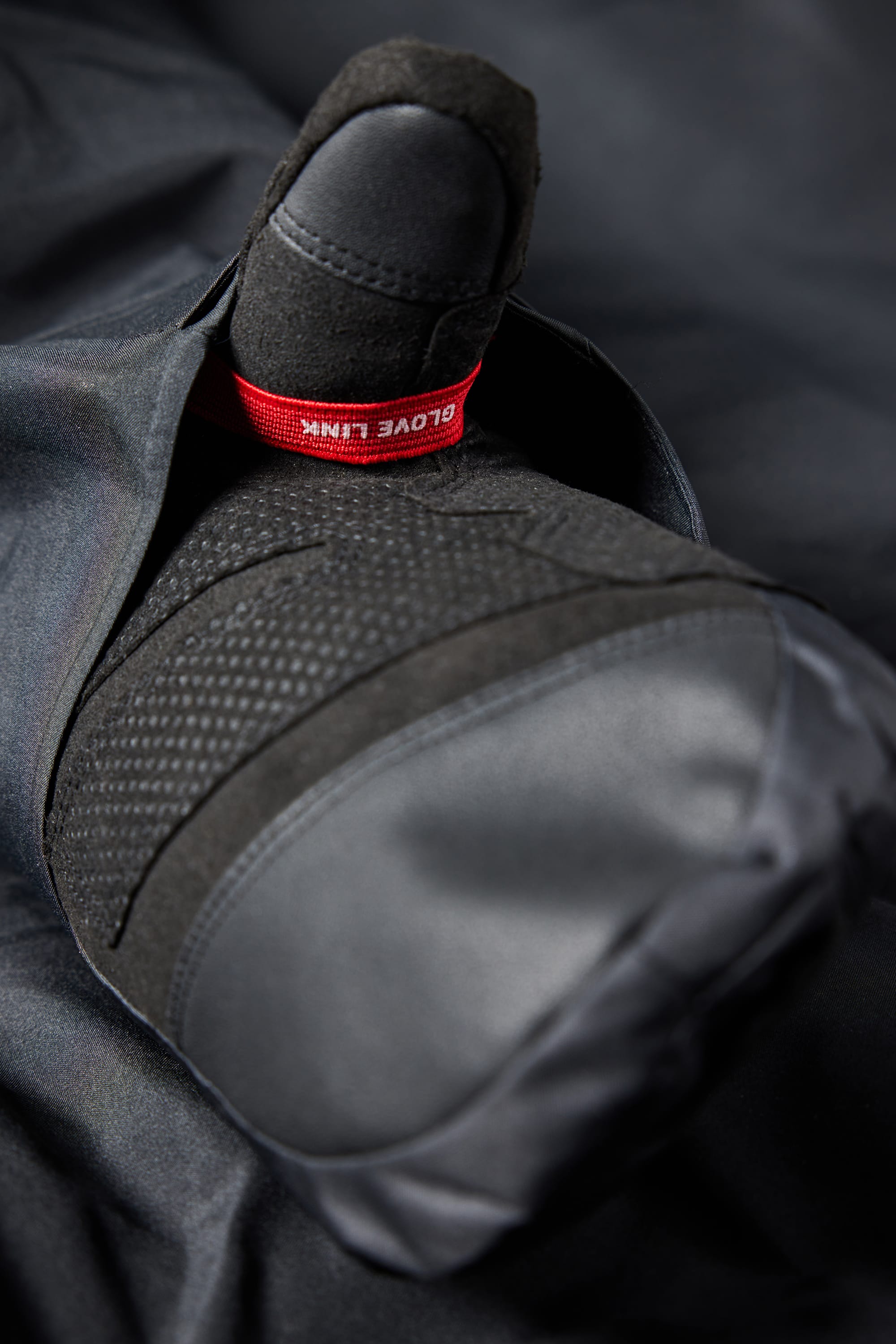 A close-up of a black gloved hand giving a thumbs up reveals a red GLOVE LINK tag near the thumb, set against dark fabric—an ideal match for your 686 Mens Waterproof Hoody by 686.