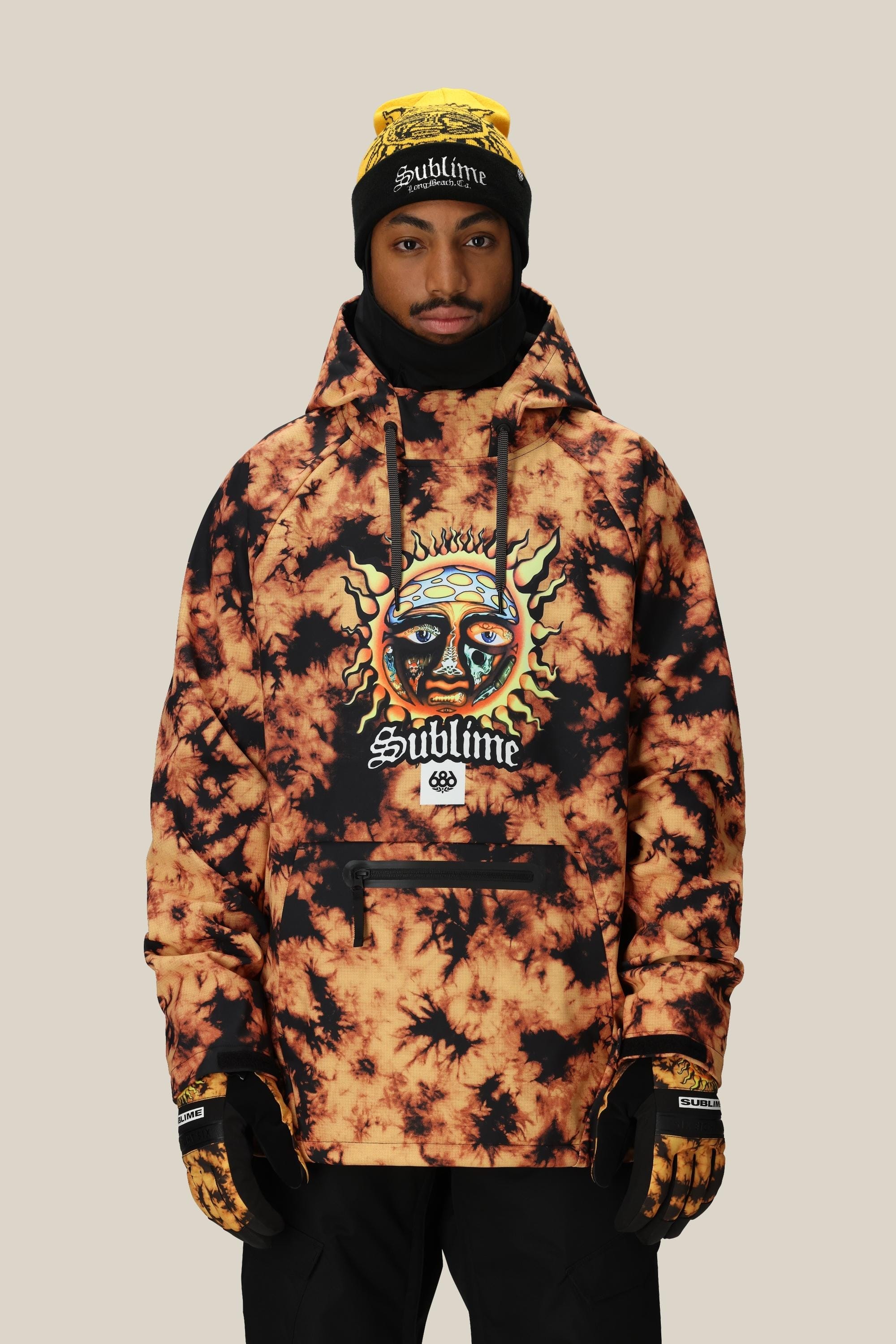 A person wearing a yellow and black 686 Mens Waterproof Hoody by 686, along with black gloves, a black ski mask, and a yellow Sublime beanie, stands against a plain beige background.