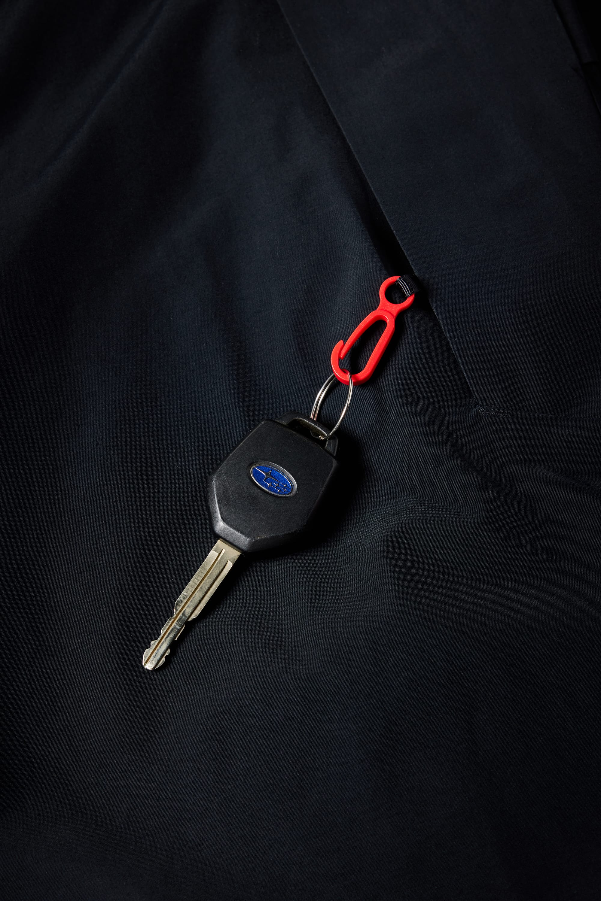 A car key with a blue oval logo and a small red carabiner clip rests on a dark 686 Mens Waterproof Hoody by 686.