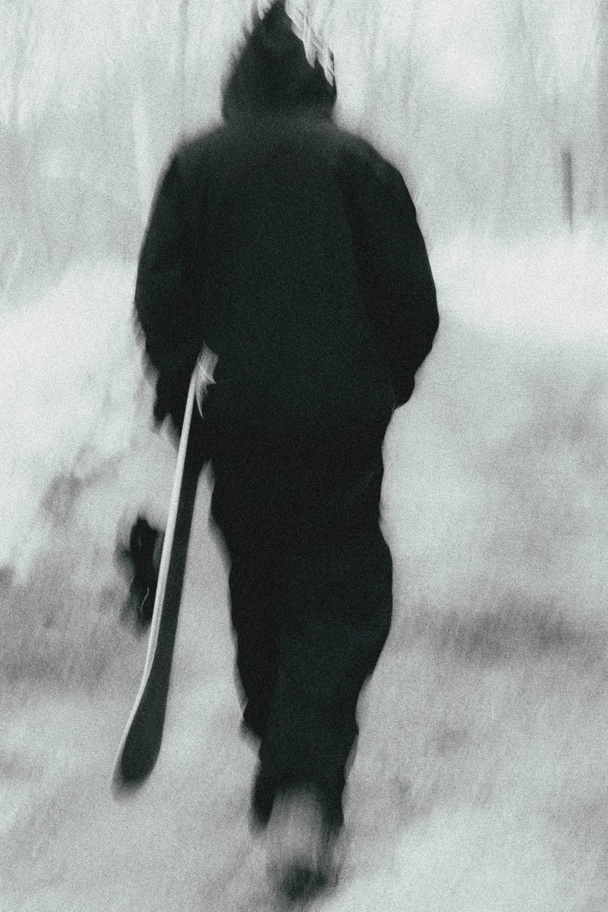Wearing the 686 Mens Waterproof Team Hoody, a figure walks away on a snowy path with a snowboard. The slightly blurred black and white photo by 686 creates a cold, wintry, and mysterious vibe.