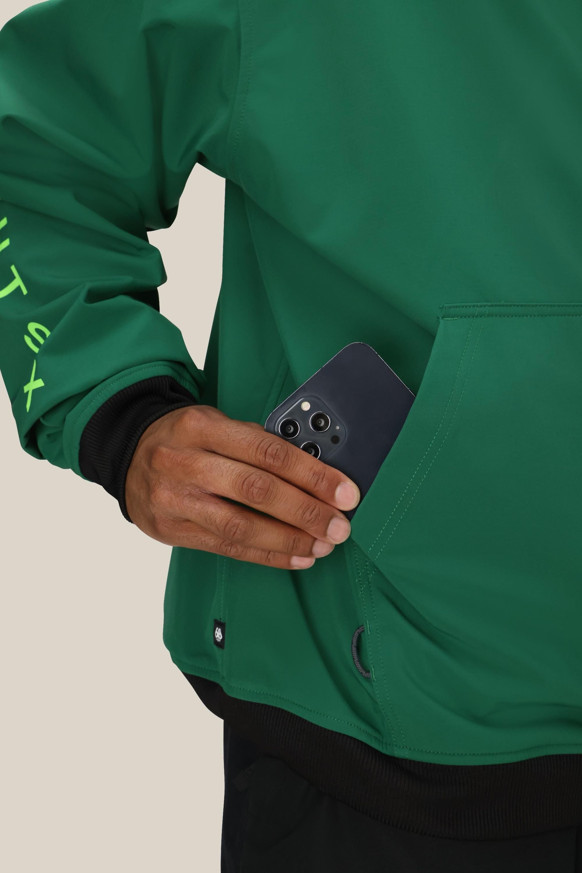 A person wearing a 686 Mens Waterproof Team Hoody is sliding a black smartphone into the front pocket; only their hand and part of their torso are visible.