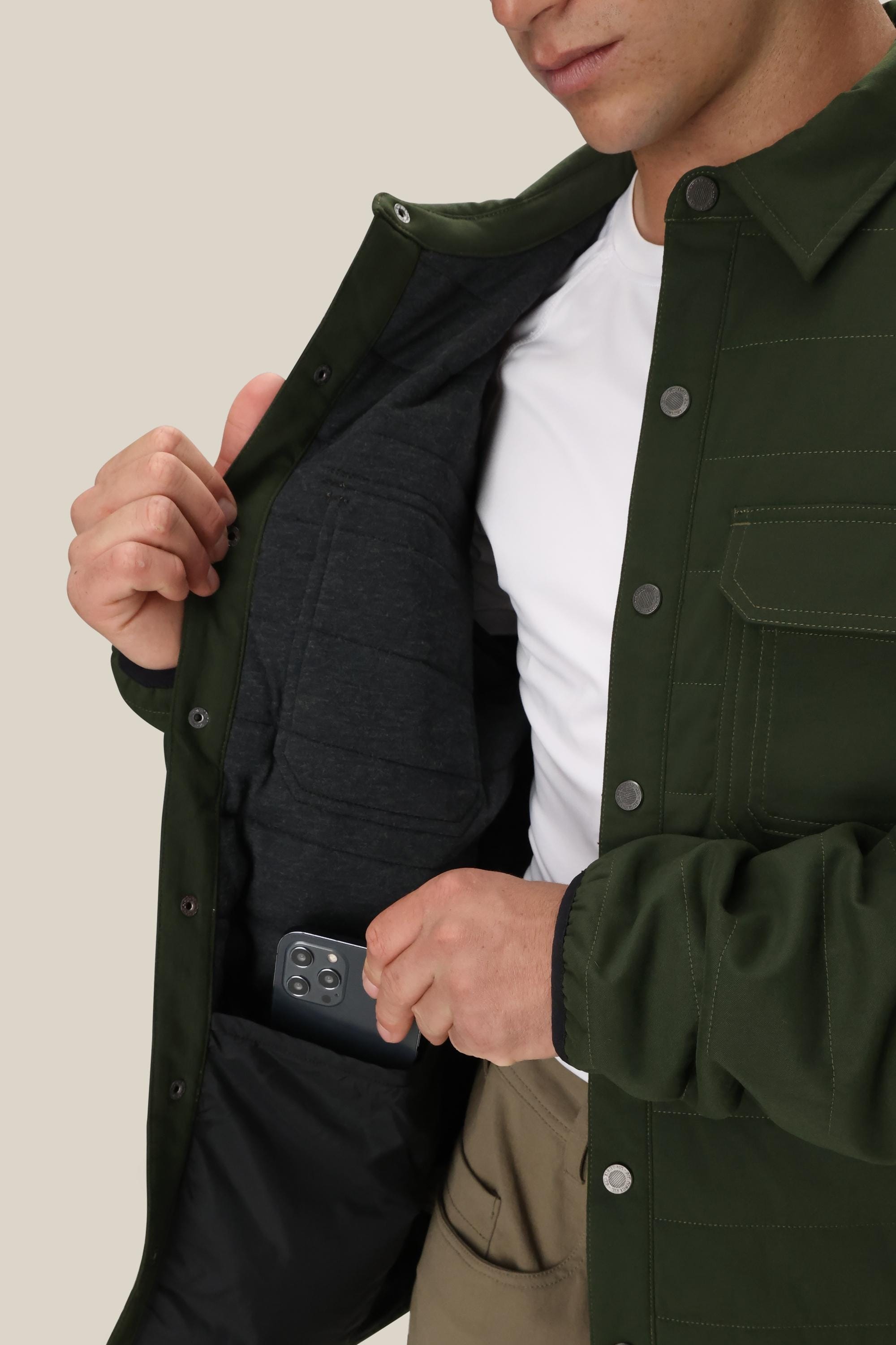 A person wearing the 686 Men's Thermaldry™ Snap-Up Shirt in green over a white shirt shows its inner pocket while placing a smartphone inside it.