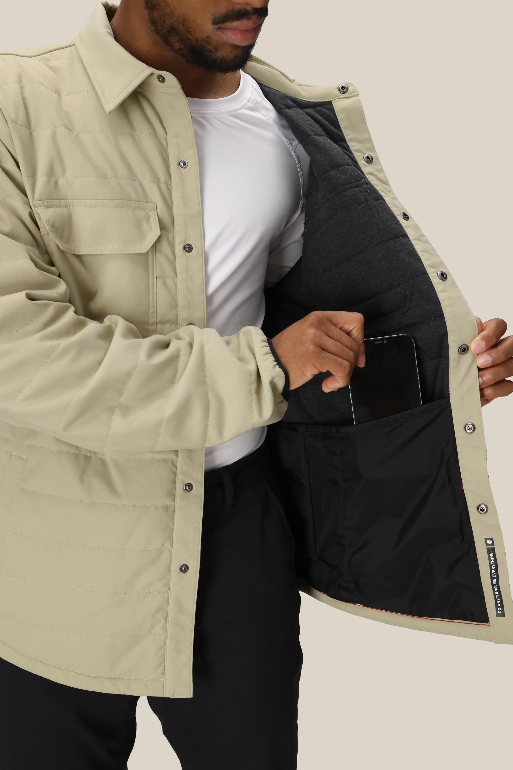 A man wearing the 686 Men's Thermaldry™ Snap-Up Shirt opens it to show a large black-lined inner pocket, placing a tablet inside. This stylish citywear piece from 686 features convenient snap buttons.