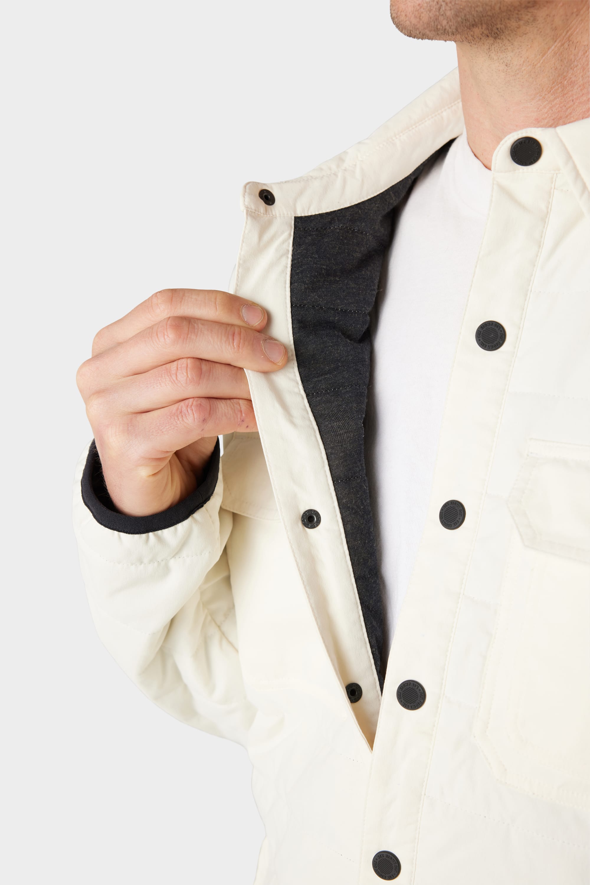 A man wears the 686 Men's Thermaldry™ Snap-Up Shirt in white, holding it open to show its dark inner lining and black snap buttons.