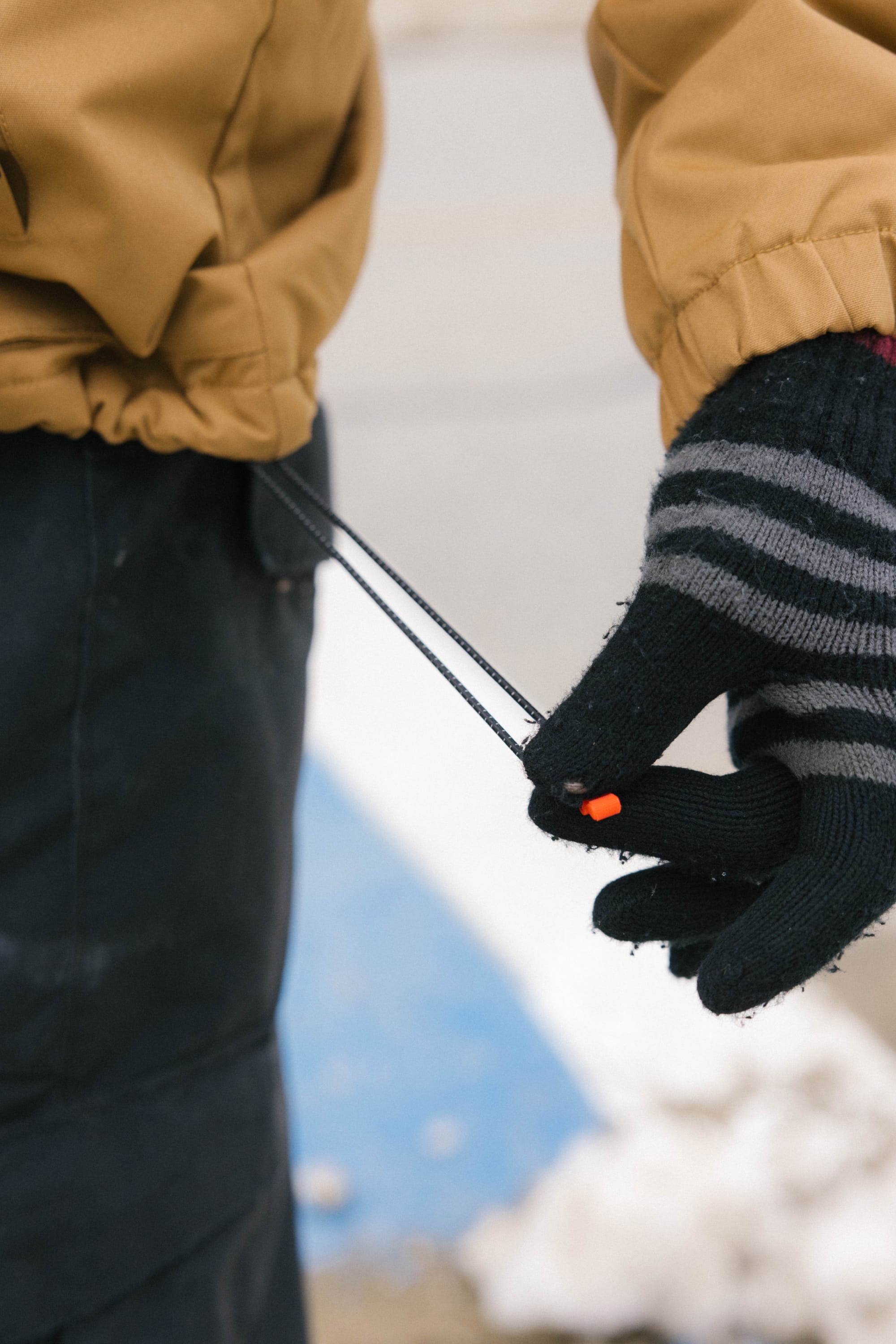 A person wearing the 686 Mens Caim Insulated Jacket adjusts the hem drawstring outdoors, with snow on the ground and black striped gloves on their hands.