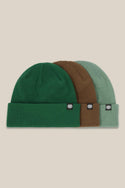 The 686 Standard Roll-Up Beanie (3-Pack) by 686 features green, brown, and light green knit beanies with a black and white logo tag on each folded brim, displayed side by side on a beige background.