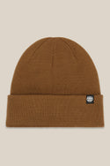 The 686 Standard Roll Up Beanie by 686 is a brown knit hat with a folded brim and a small black-and-white rectangular logo tag on the cuff, shown against a light beige background.