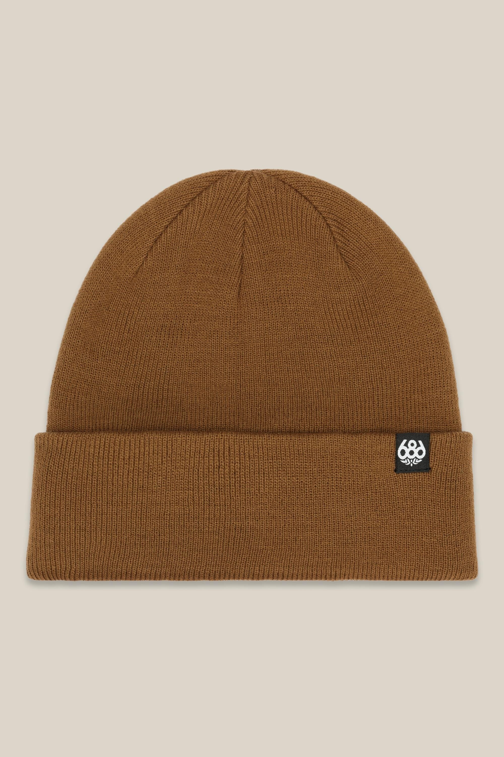 The 686 Standard Roll Up Beanie by 686 is a brown knit hat with a folded brim and a small black-and-white rectangular logo tag on the cuff, shown against a light beige background.