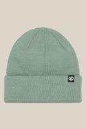 The 686 Standard Roll Up Beanie by 686 is a light green knit hat with a wide folded cuff and a small black rectangular tag with a white logo on the left side of the cuff, shown on a beige background.