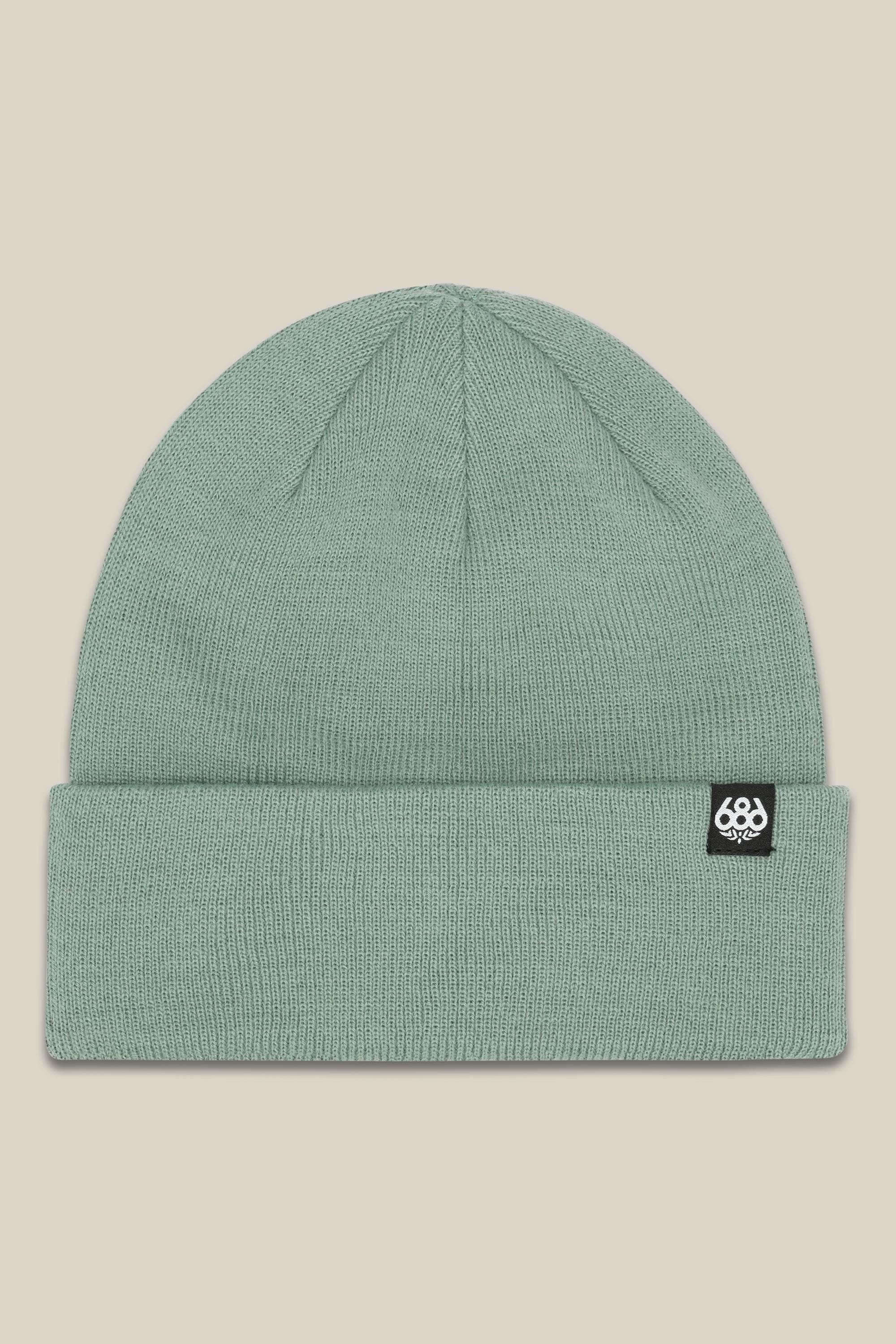 The 686 Standard Roll Up Beanie by 686 is a light green knit hat with a wide folded cuff and a small black rectangular tag with a white logo on the left side of the cuff, shown on a beige background.