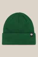 The 686 Standard Roll Up Beanie by 686 is a green knit hat with a folded brim and a black-and-white rectangular 686 logo tag on the cuff, shown against a light beige background.