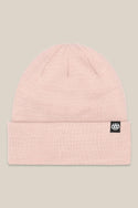 The 686 Standard Roll Up Beanie is a light pink knit hat with a folded brim and a small black tag featuring the white 686 logo on the left side, shown against a beige background.