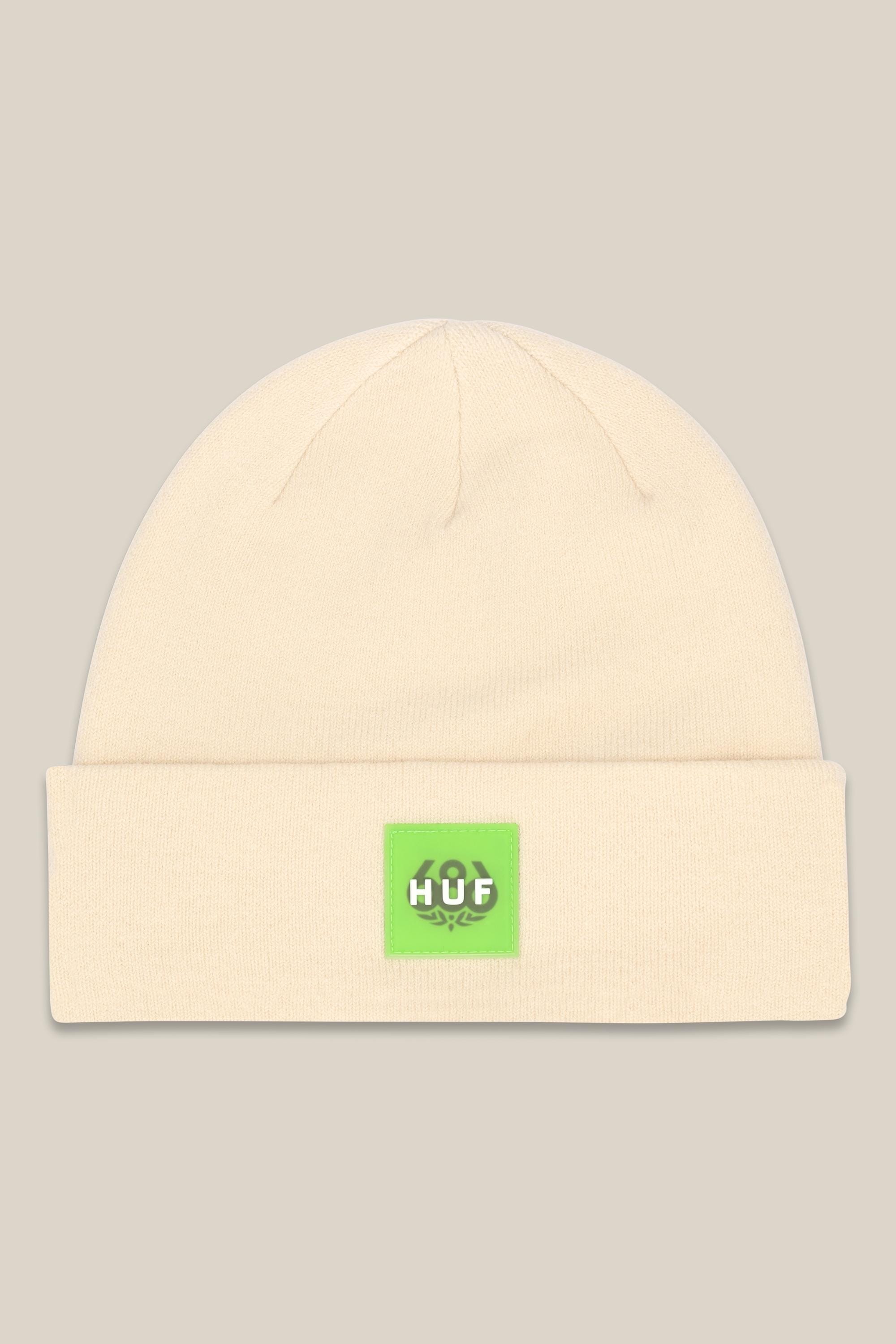 The 686 HUF Beanie by 686 is a cream mid-weight cuffed beanie with a folded brim, featuring a bright green front patch displaying the white HUF logo and a small graphic.