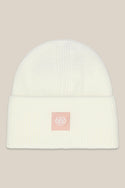 The 686 Big Cuff Beanie by 686 is a white ribbed knit hat with a folded brim and a small pink embroidered 686 patch on the front. Stylish autumn headwear, shown against a solid beige background.