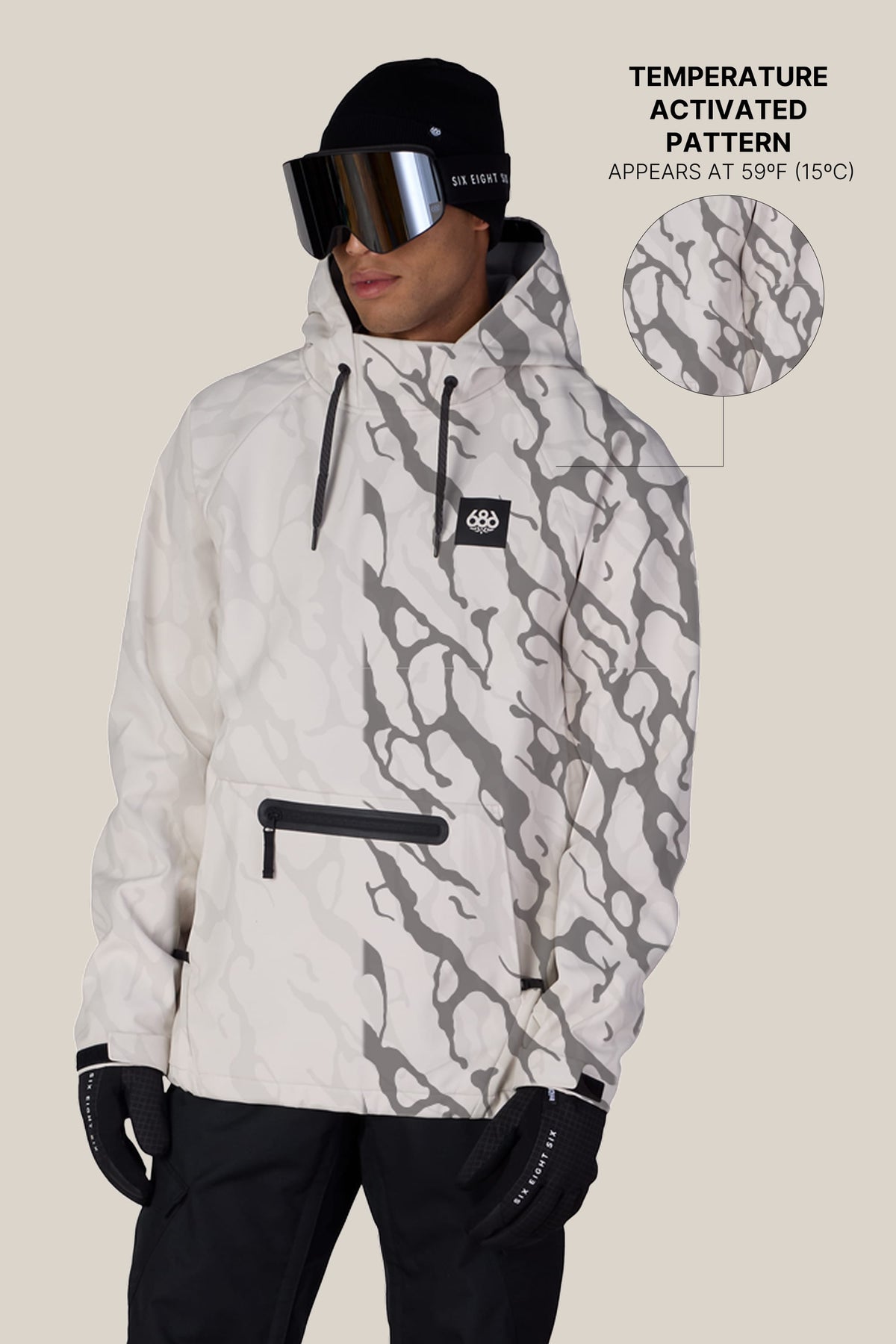 A person wears the 686 Men’s Waterproof Hyperchromic Pullover Hoody, featuring a white color with gray patterns, along with black pants, gloves, and goggles. Text explains that the pattern on the 686 hoody becomes visible at 59°F (15°C) due to its temperature-activated design, accompanied by a close-up of the pattern detail.