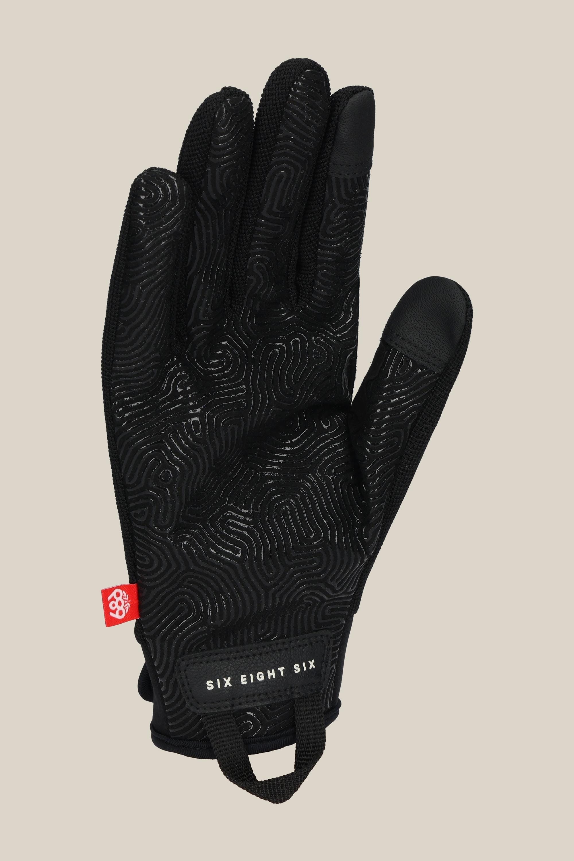 The 686 Outlaw Pipe Glove by 686 features a black design with subtle palm textures, a red side tag, and "SIX EIGHT SIX" printed on the cuff, shown against a neutral beige background.