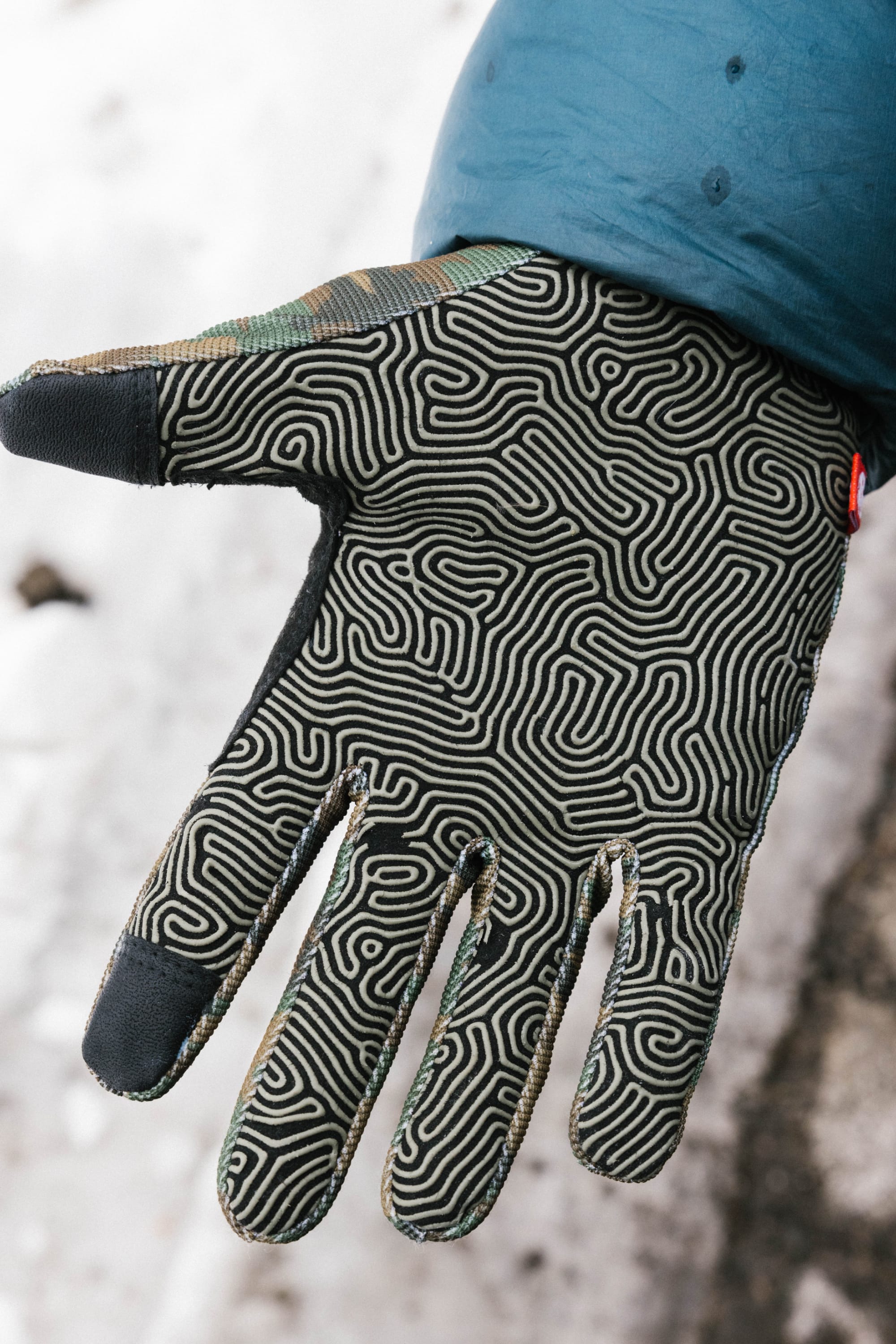 A gloved hand extends outward, wearing the 686 Outlaw Pipe Glove by 686, featuring an intricate black and white maze pattern. The person is dressed in a blue jacket with a snowy background.