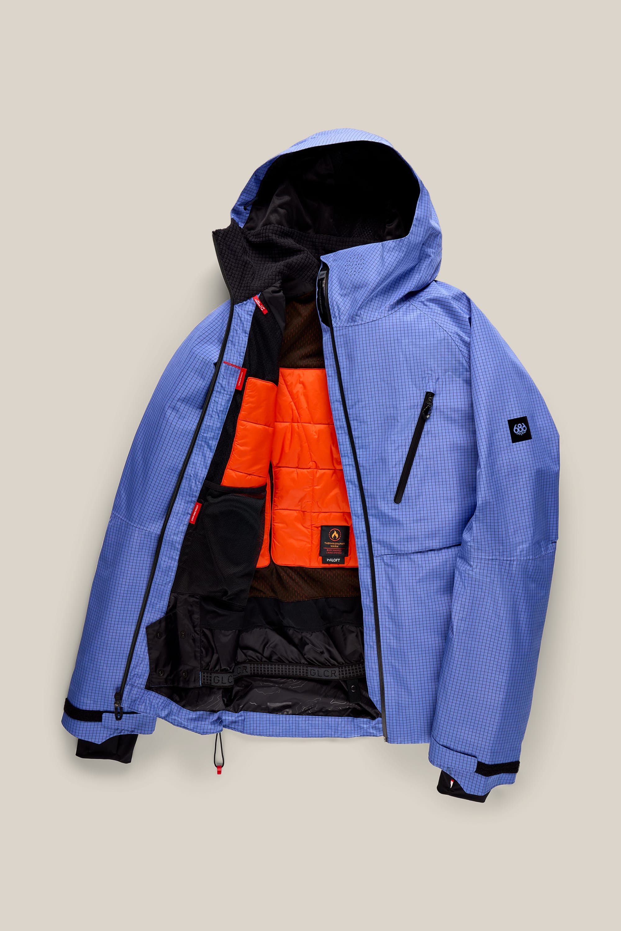 The 686 Men’s Hydra™ Thermagraph® Jacket by 686, in blue with a black zipper, is laid open on a beige background, showcasing its vibrant orange inner lining and black interior pockets.