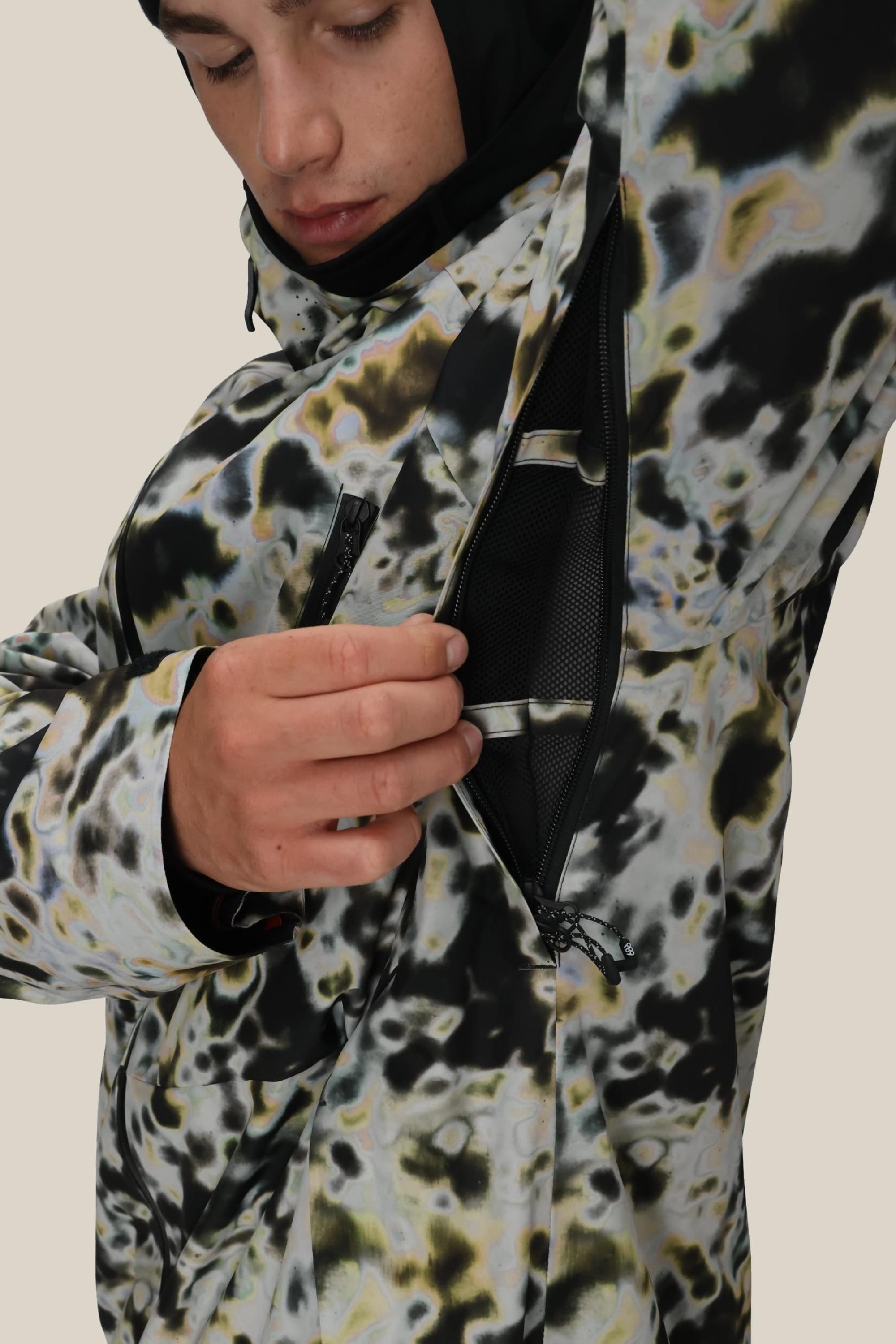 A person wearing the 686 Men's Hydra™ Thermagraph® Jacket unzips a side vent, revealing black mesh body-mapped lining inside. The background is plain and neutral.