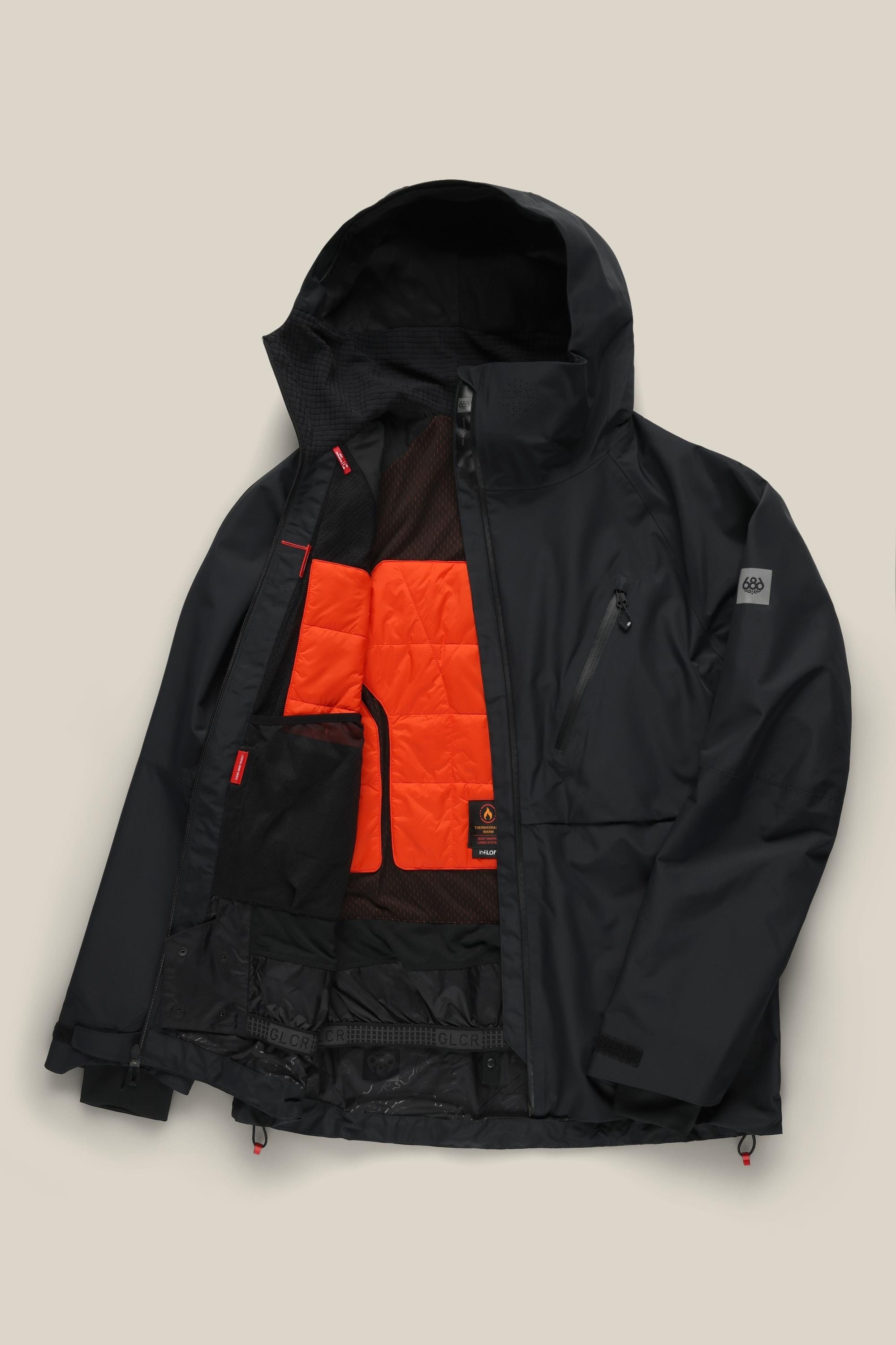 The 686 Men’s Hydra™ Thermagraph® Jacket by 686 is shown in black, laid flat and partially unzipped to display its orange and black inner lining, interior pockets, and mesh panels.