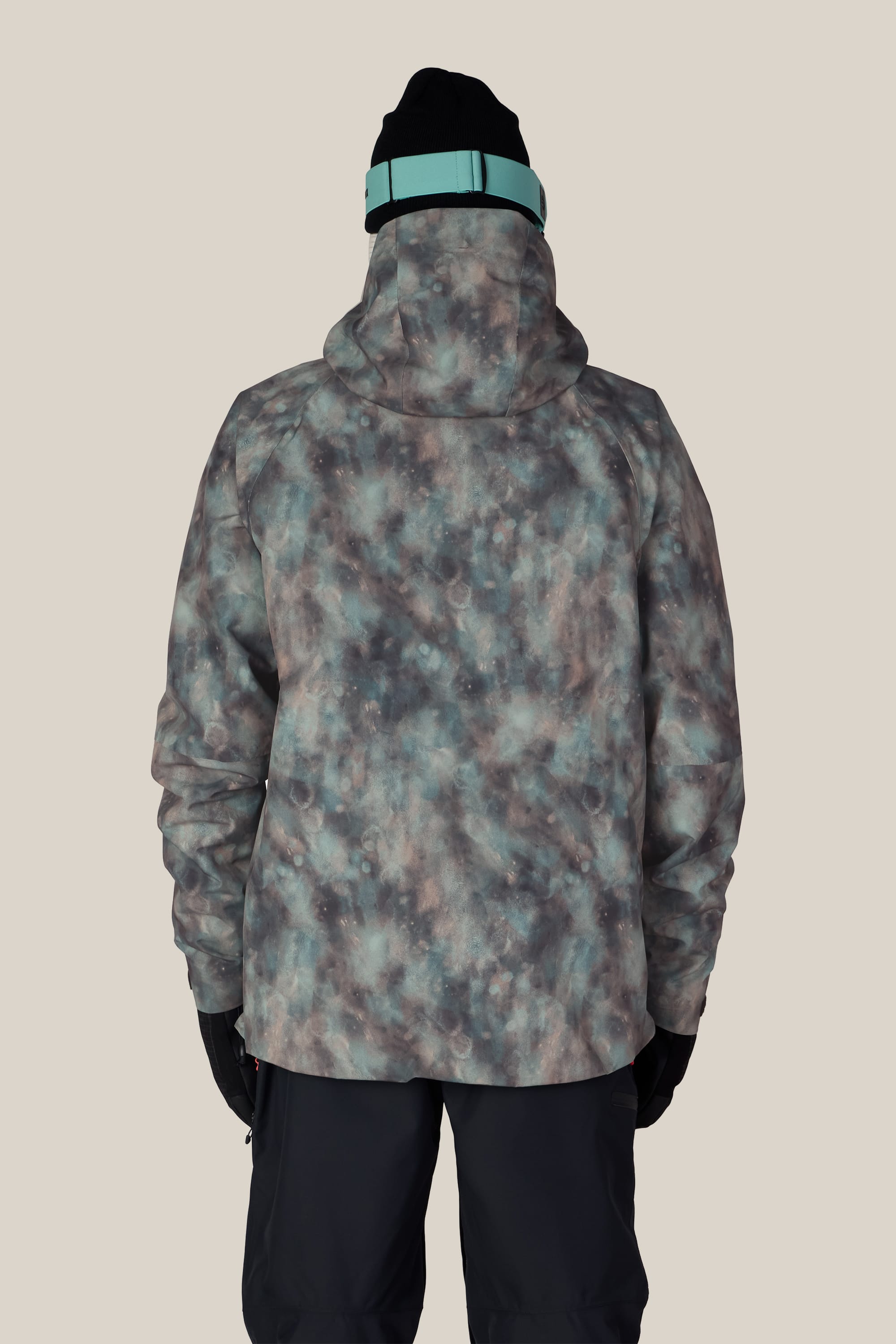A person is shown from the back against a plain light background, wearing the 686 Men’s Hydra™ Thermagraph® Jacket by 686—a blue and grey patterned jacket—paired with black gloves, dark pants, and a black beanie featuring a teal strap.