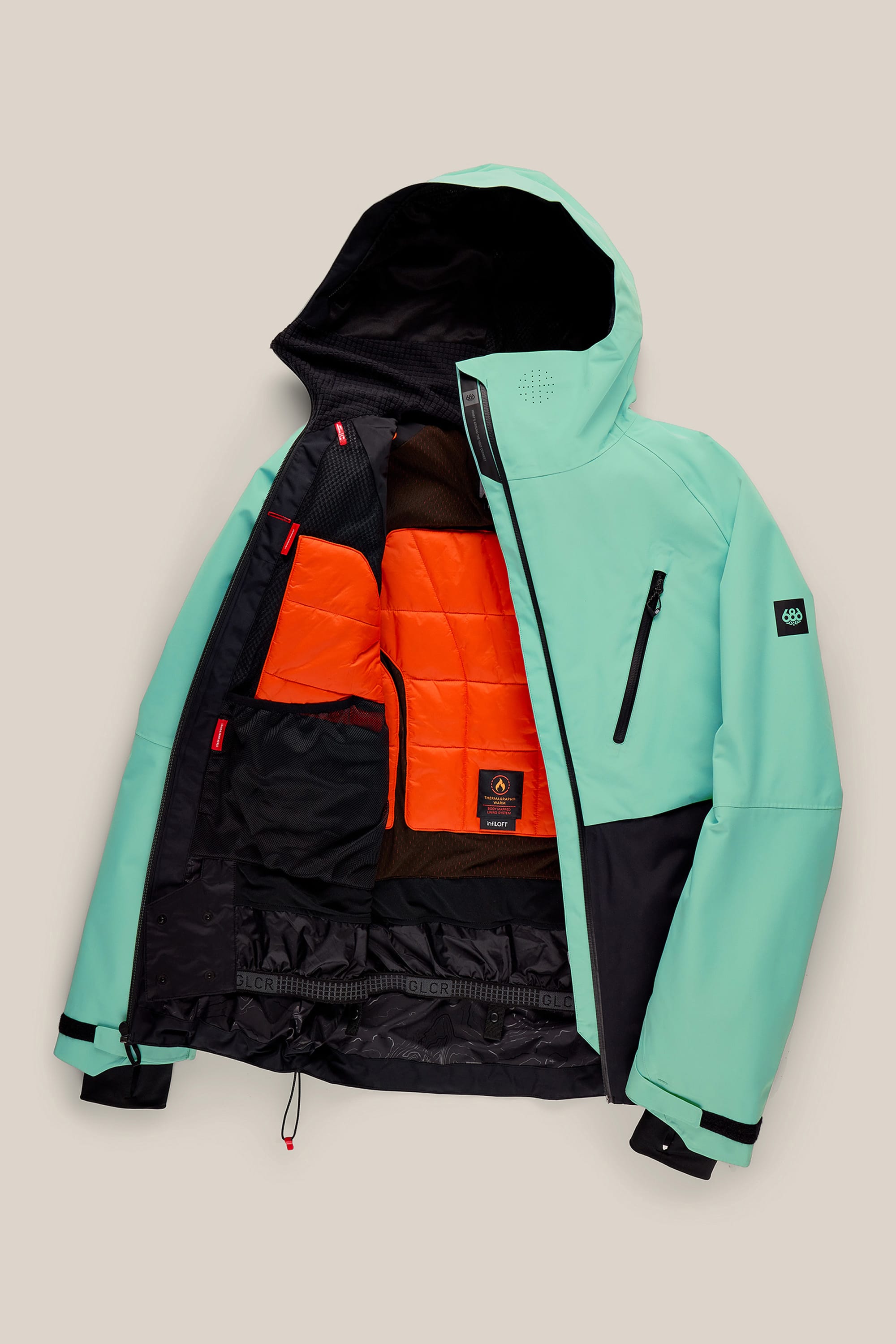 The 686 Men’s Hydra™ Thermagraph® Jacket by 686 is displayed open against a beige background, featuring a mint green and black exterior with an orange insulated lining, black mesh pockets, and detailed interior accents.