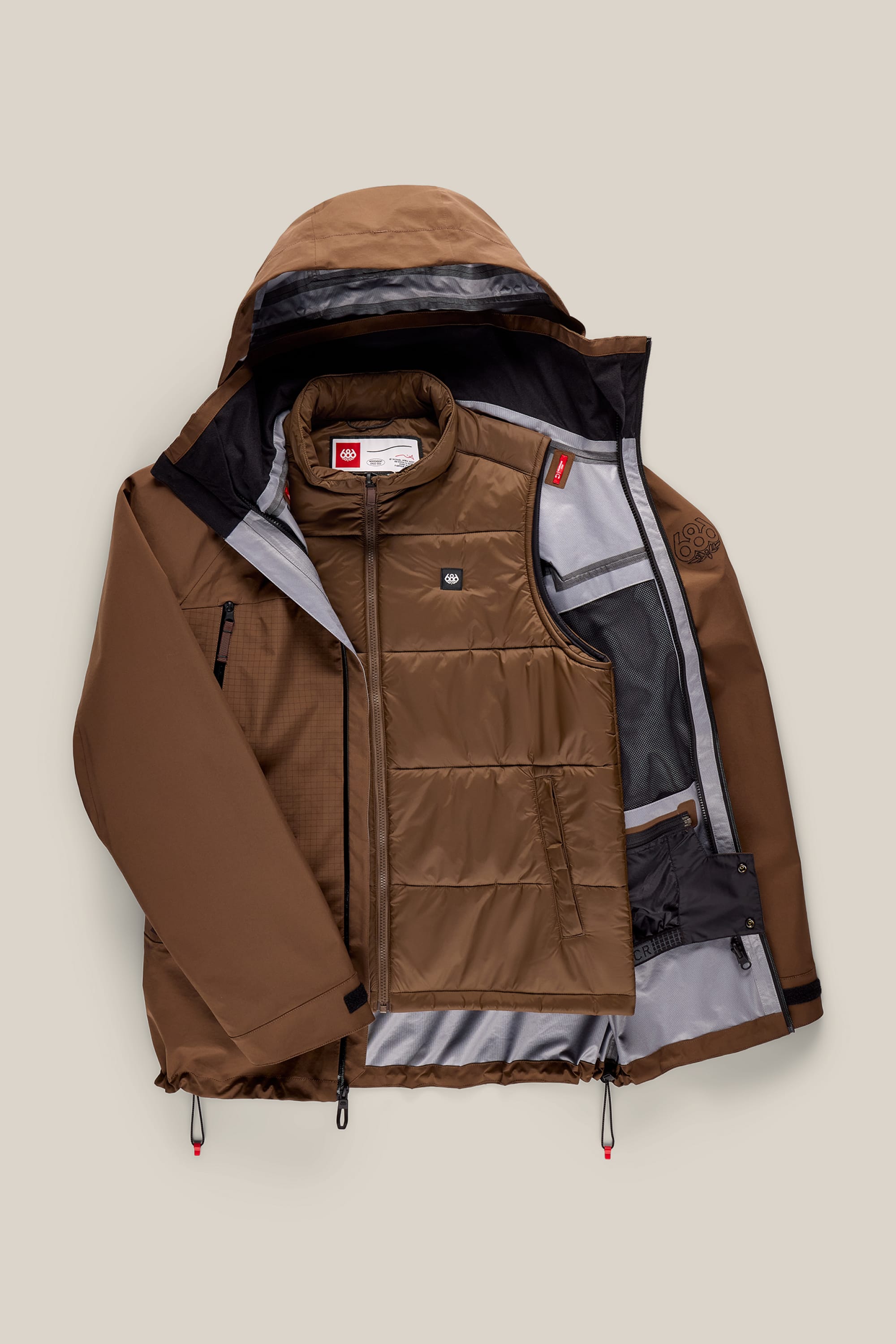 The 686 Men’s SMARTY® 3-In-1 Rodeo™ 3L Jacket by 686, shown in brown with a hood and unzipped to reveal a quilted inner vest and multiple interior pockets, set against a light beige background.