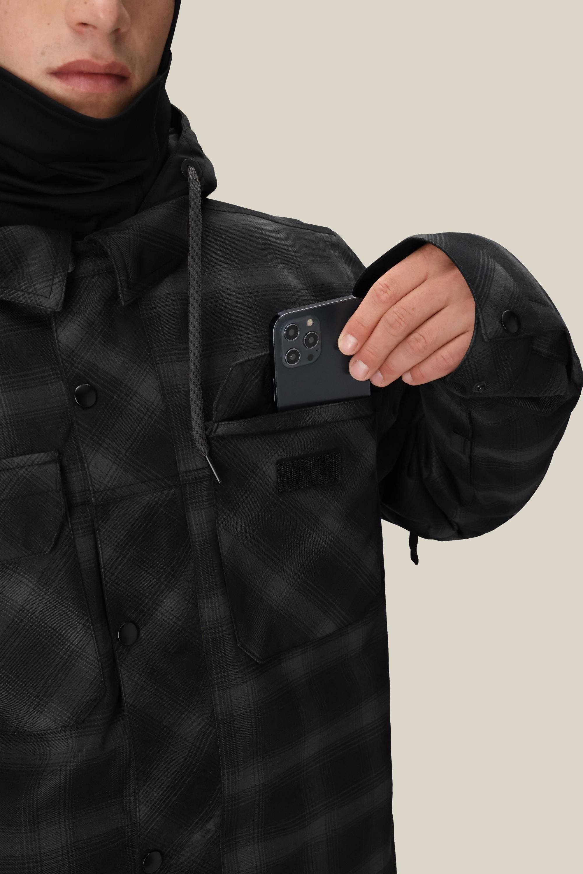 A person wearing the 686 Men's Woodland™ Insulated Jacket is putting a black smartphone into the left chest pocket. The person's face is partially visible, with a plain, light-colored background.