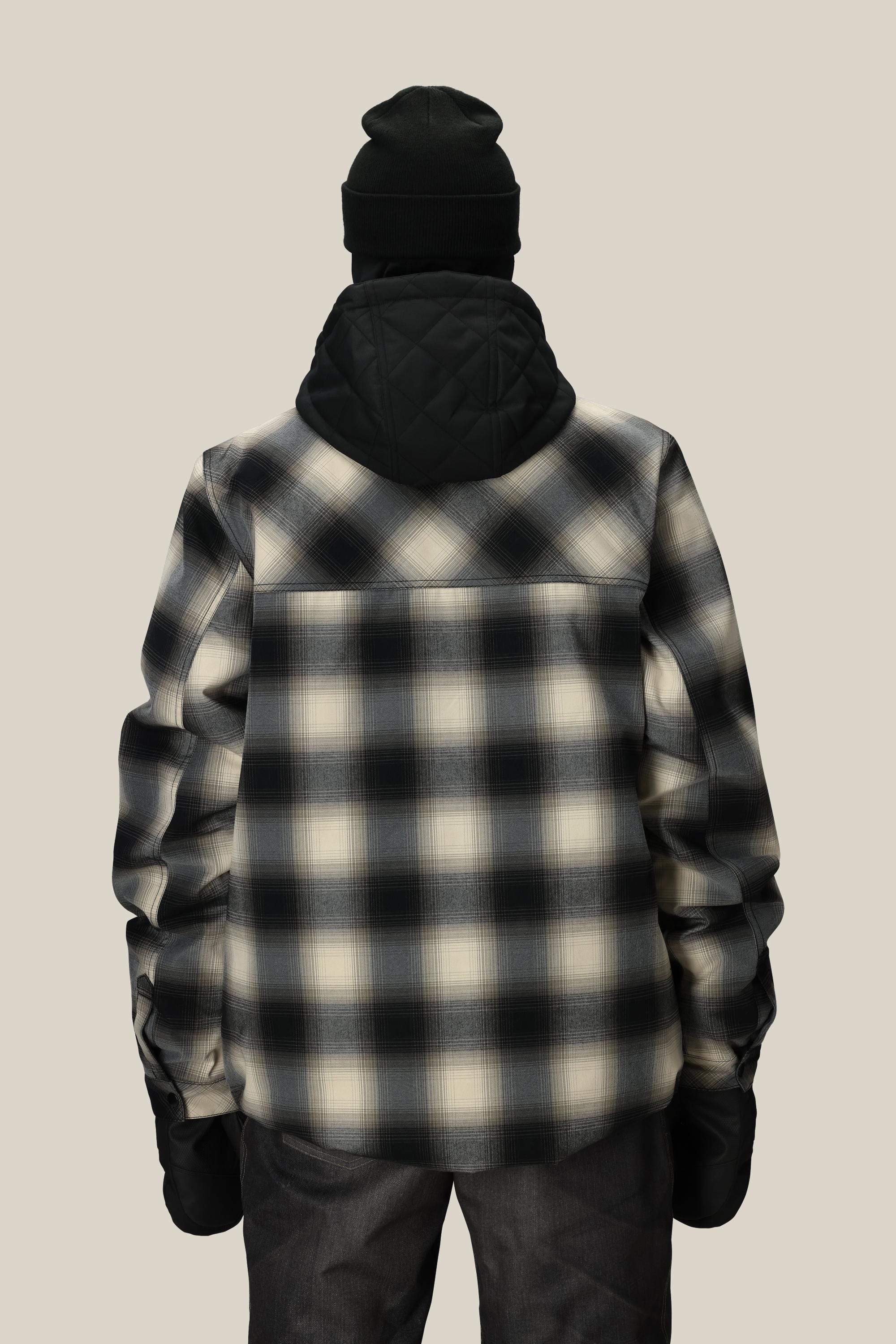 A person is seen from the back against a plain beige background, wearing the 686 Men’s Woodland™ Insulated Jacket—a black and white plaid, hooded jacket from 686—paired with a black beanie and dark pants.